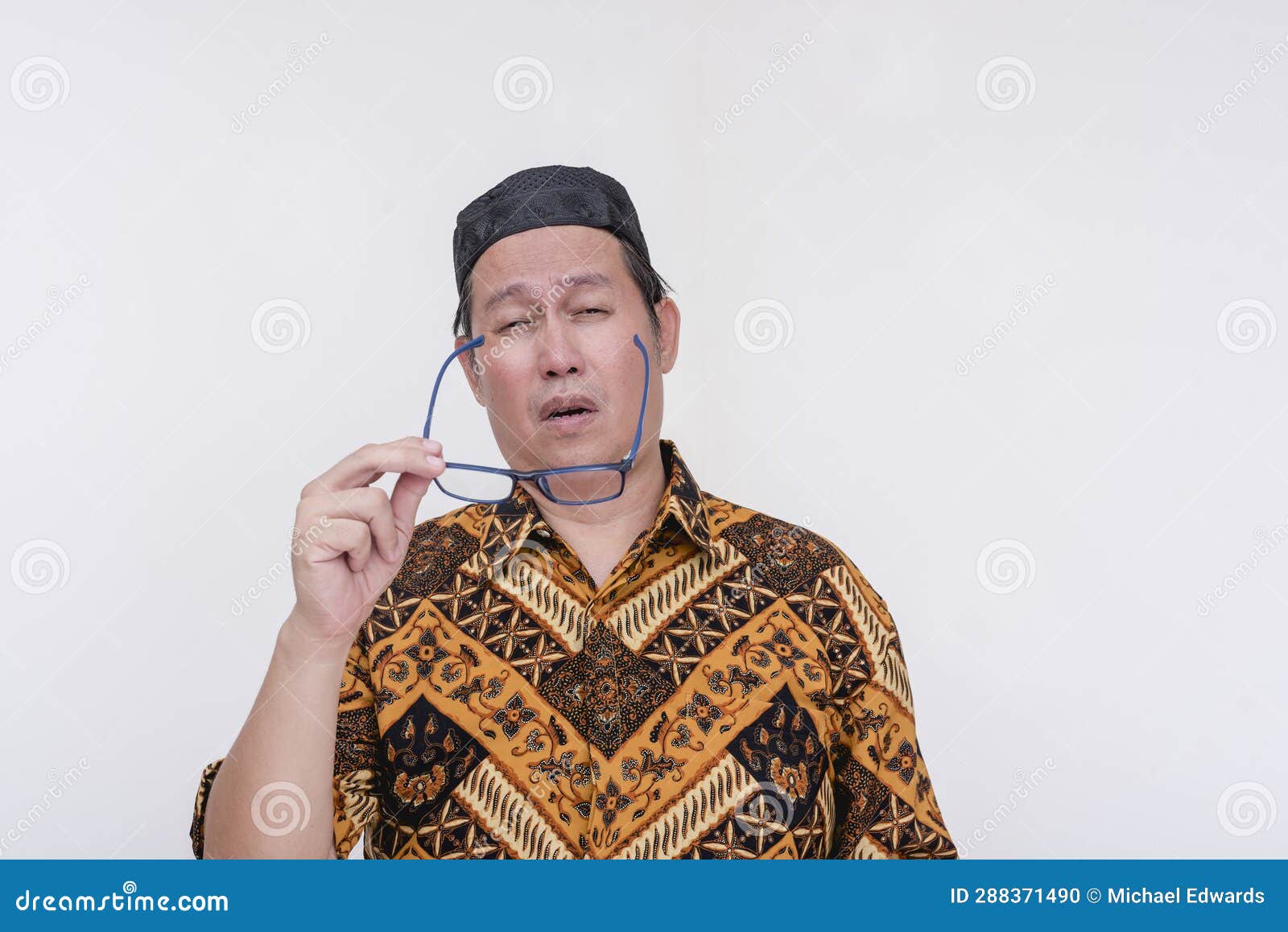a groggy and stressed middle aged man takes off his glasses after feeling eyestrain. an overworked person wearing a batik shirt