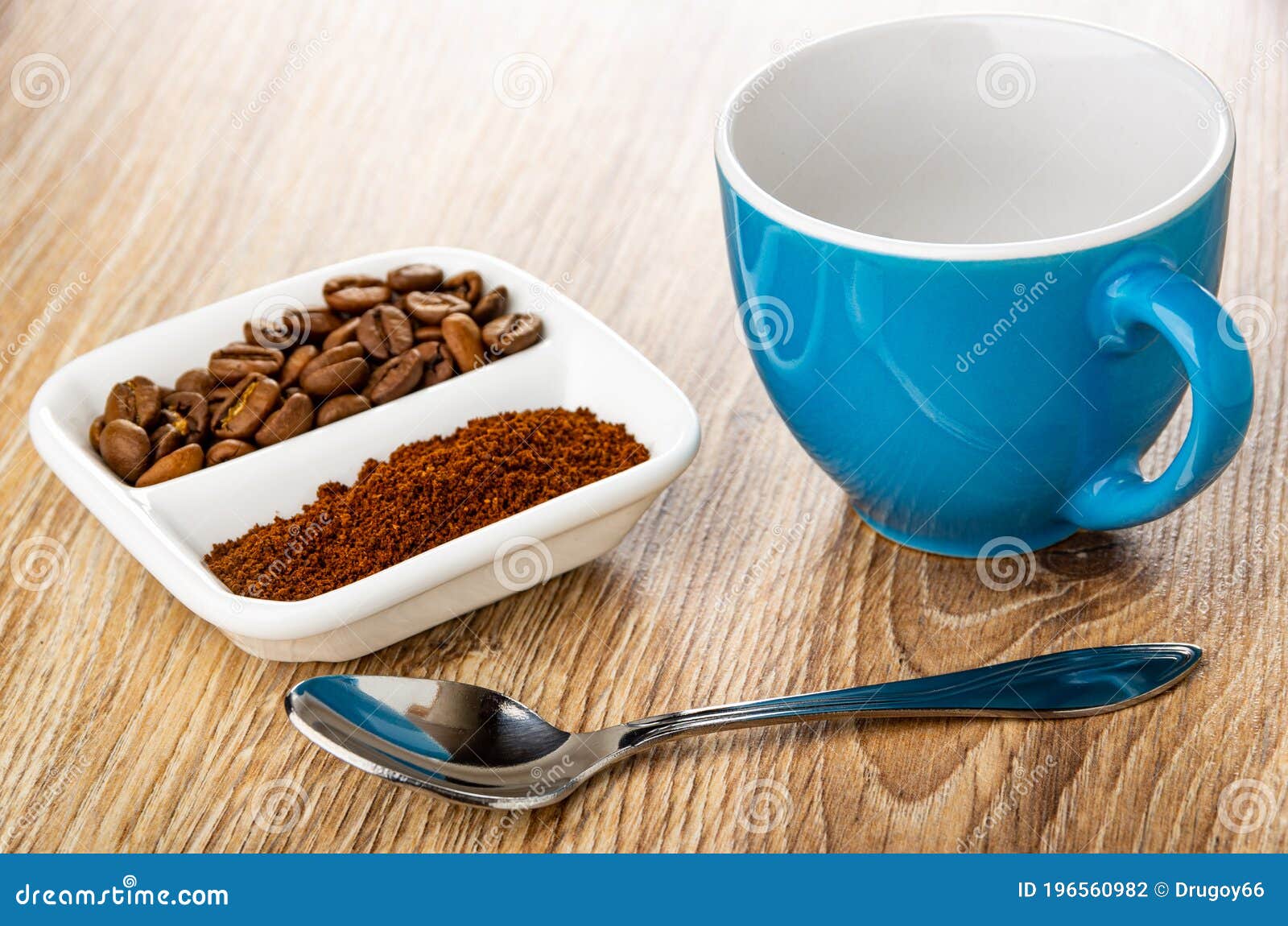 ground coffee and coffee beans in partitioned bowl, empty coffee cup, spoon on wooden table