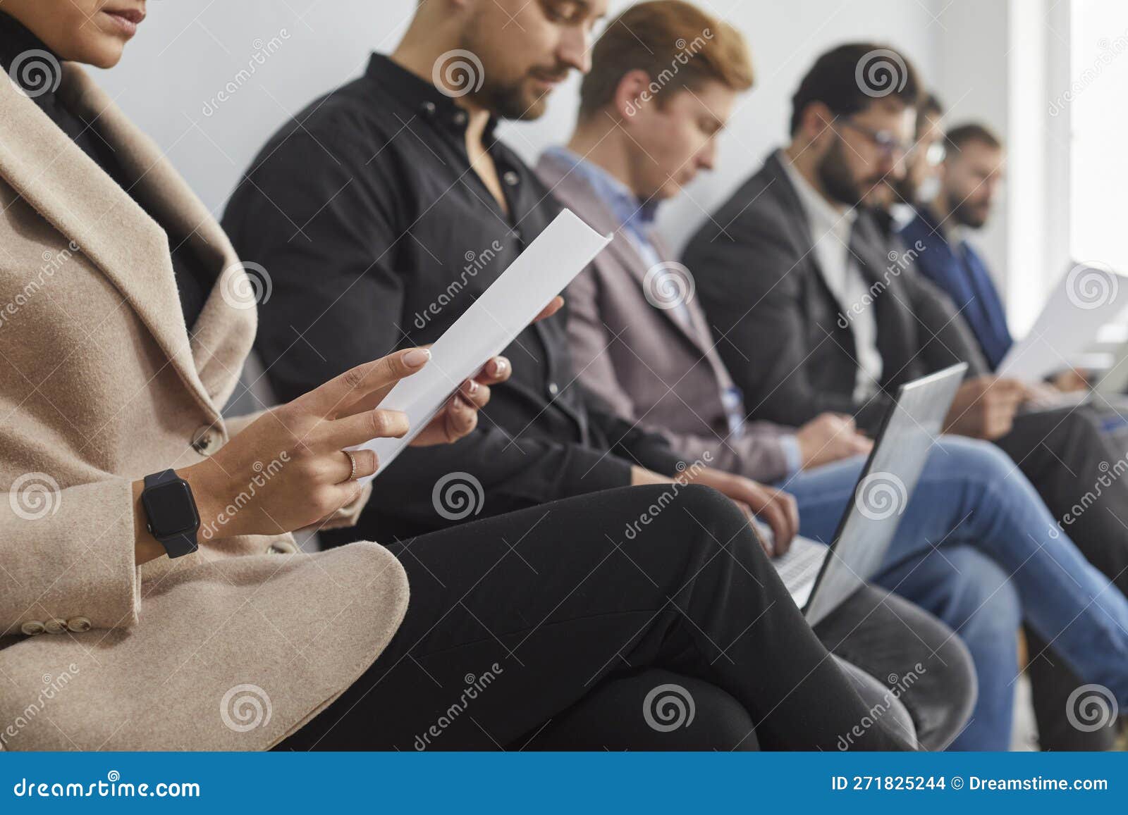group of candidate are sitting on chairs in a queue, waiting for an interview, holding questionnaires, laptops and
