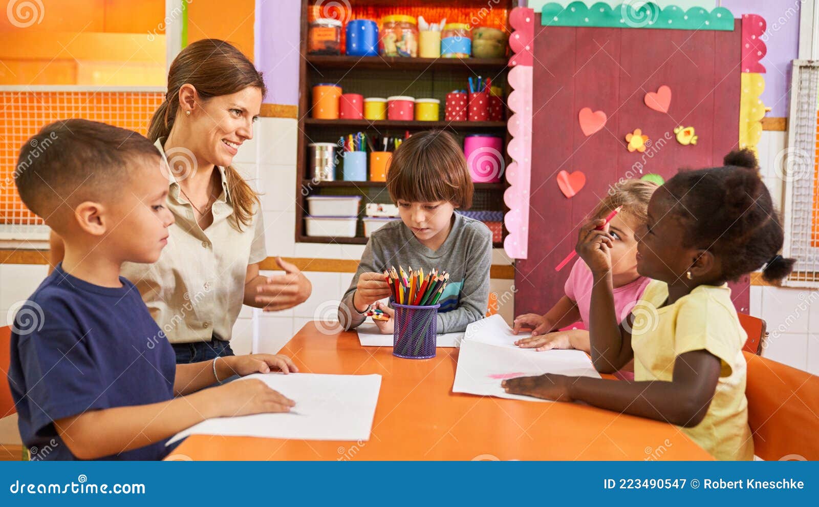 Group of Children Paints with Crayons in Daycare with an Educator Stock