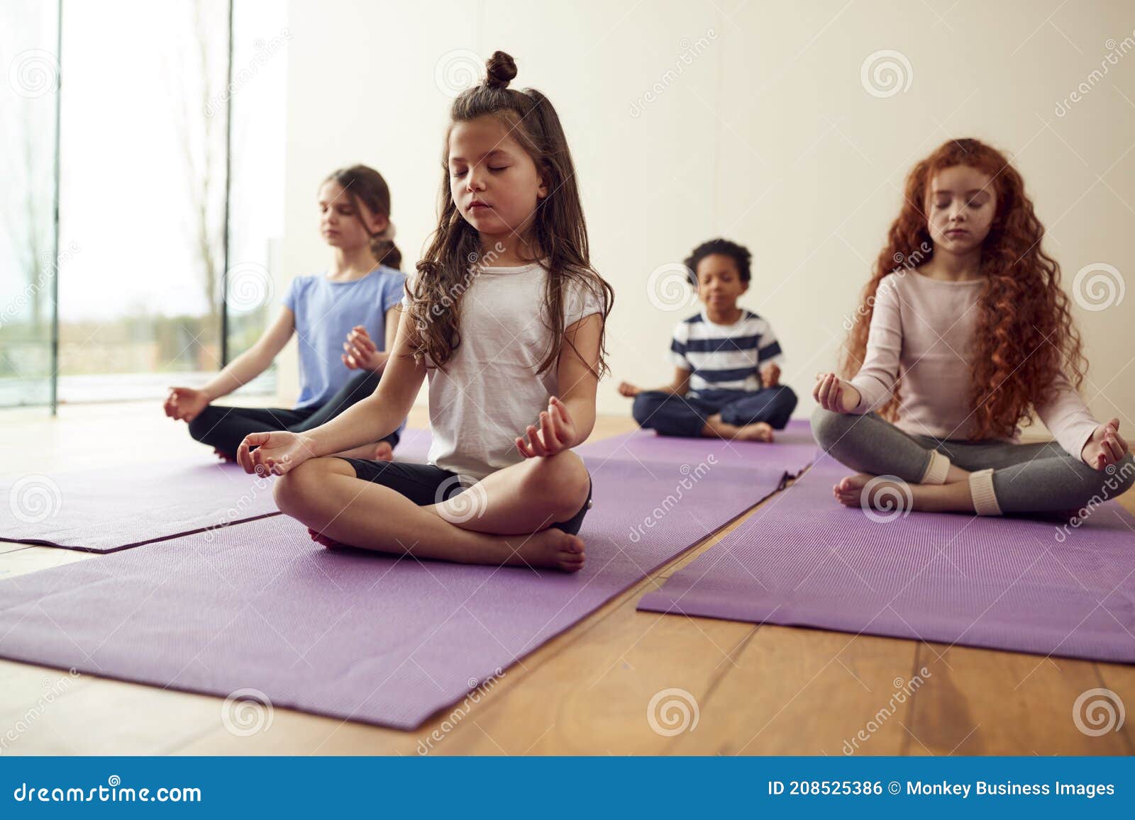 group of children sitting on exercise mats and meditating in yoga studio