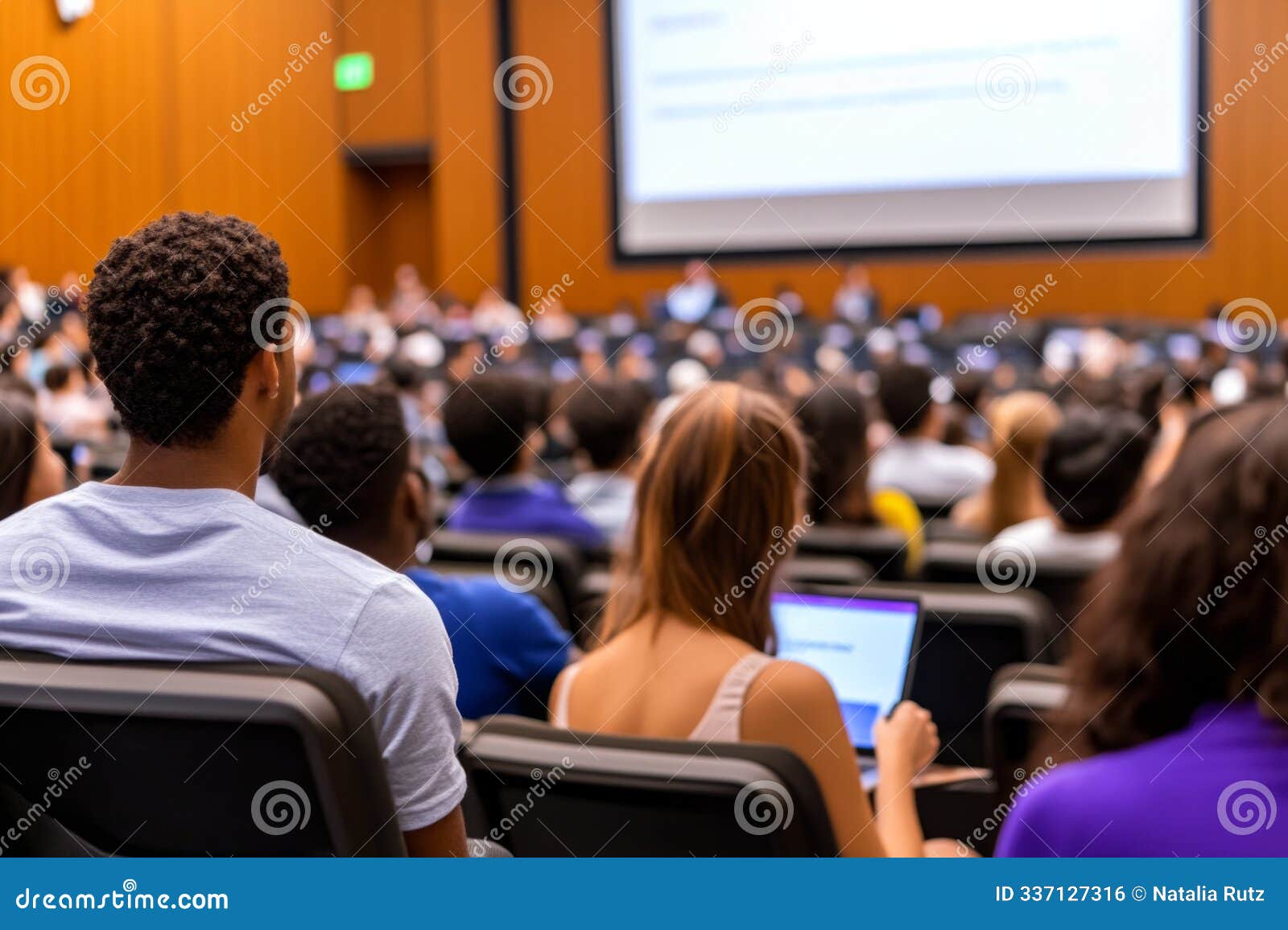 a group of diverse university students attentively listen to a lecture in a large hall.