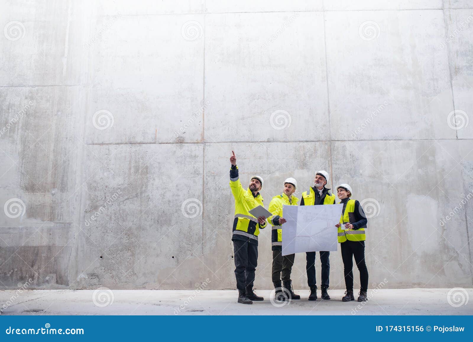 A Group Of Engineers Standing Against Concrete Wall On Construction