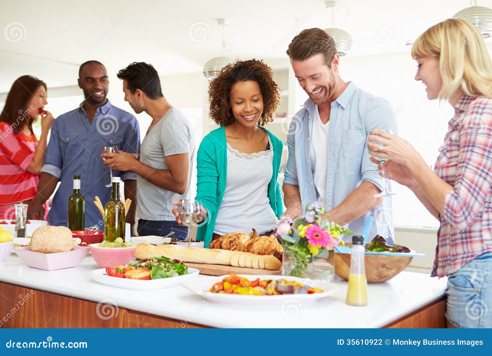 group friends having dinner party home kitchen chatting to each other whilst eating food 35610922