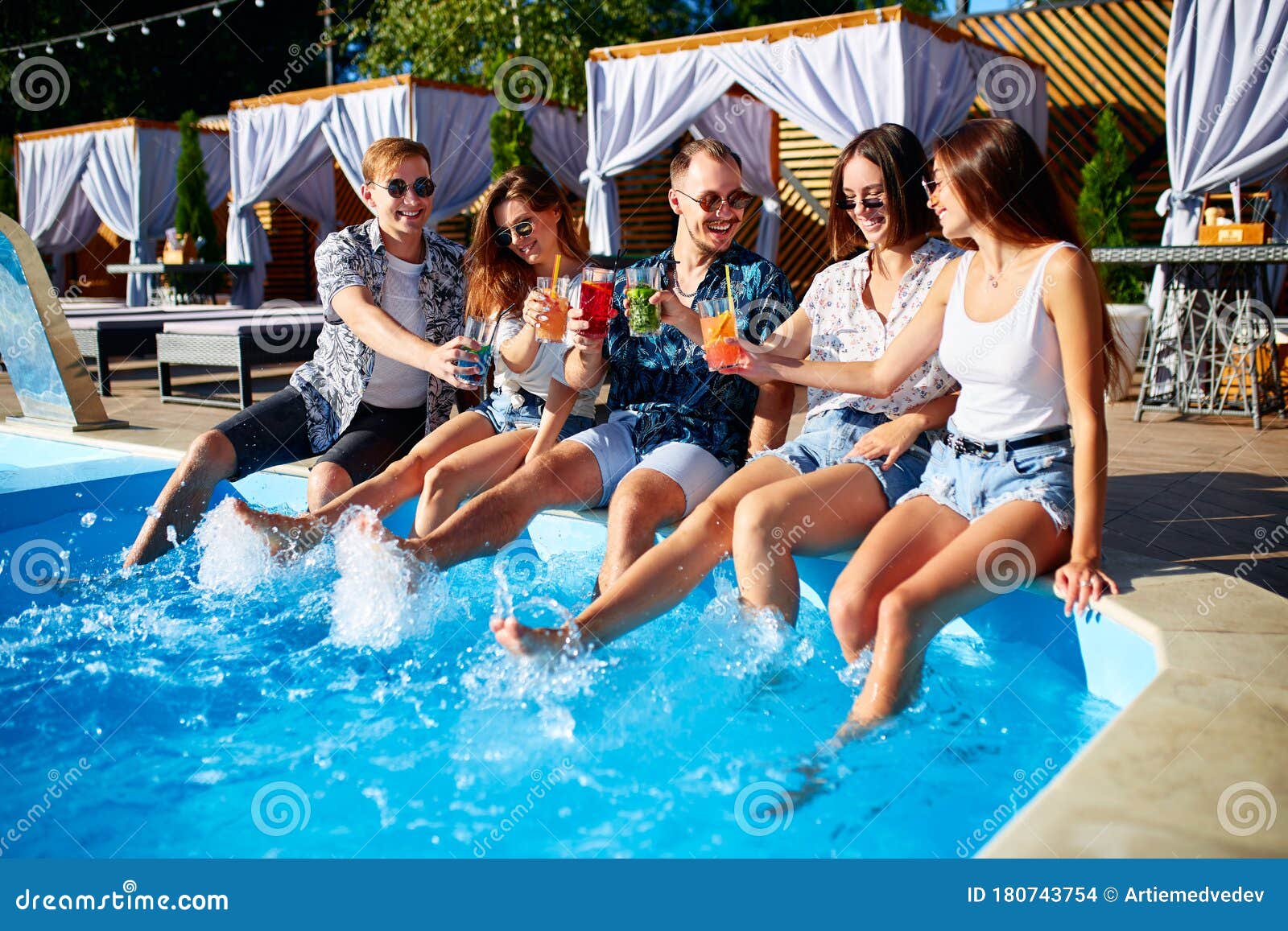 Group Of Friends Having Fun At Poolside Party Clinking Glasses With Fresh Cocktails Splashing