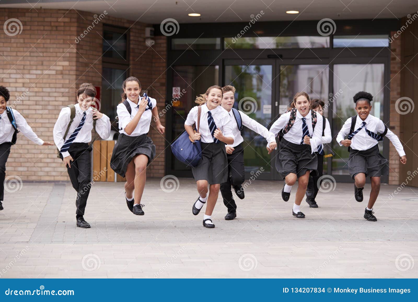 group of high school students wearing uniform running out of school buildings towards camera at the end of class
