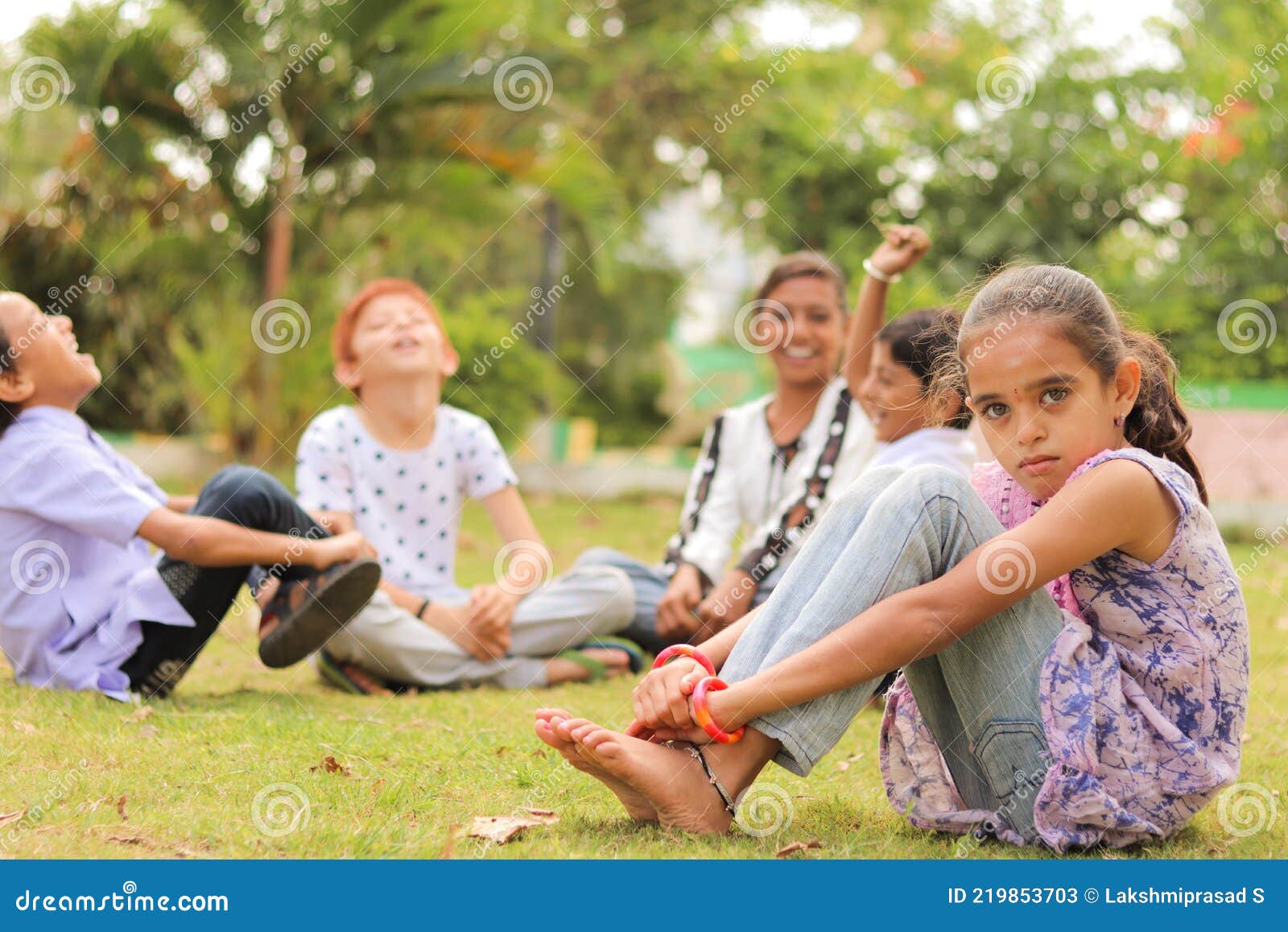 group of kids bulling girl at park during summer camp - little girl looking camera, sitting lonely while friends playingand having