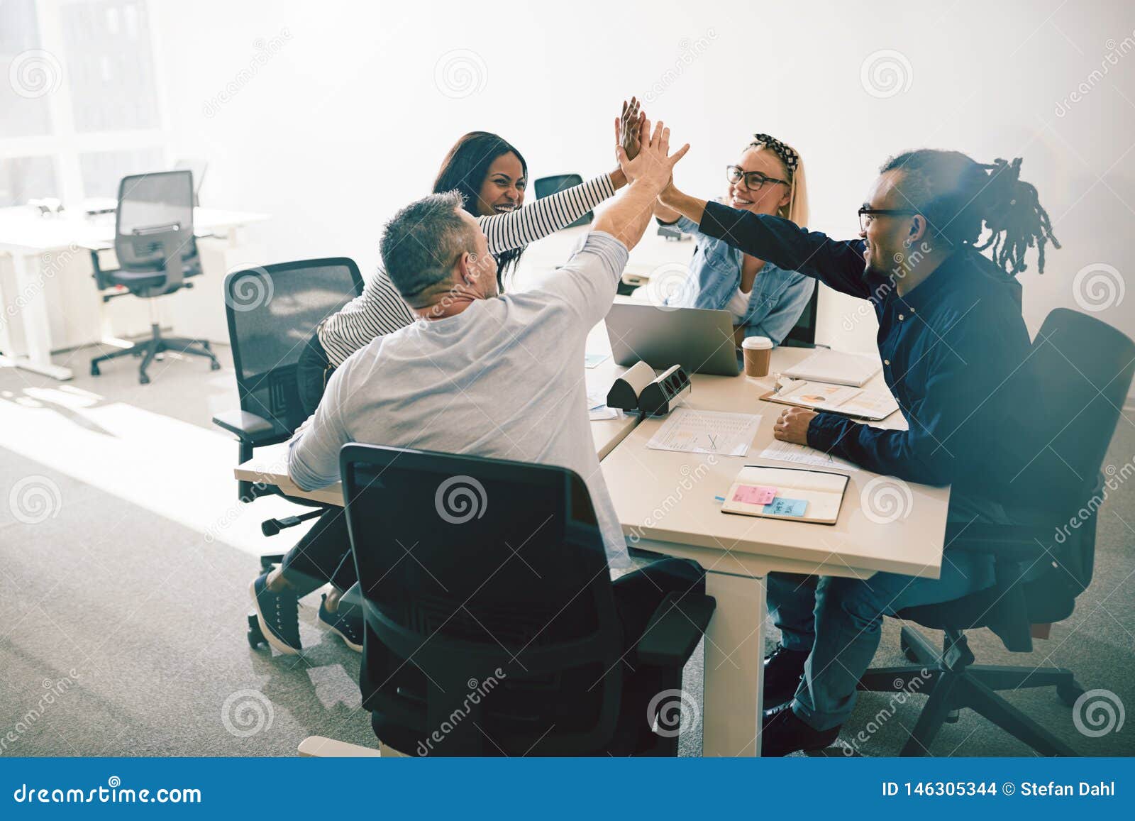 group of laughing coworkers high fiving during an office meeting
