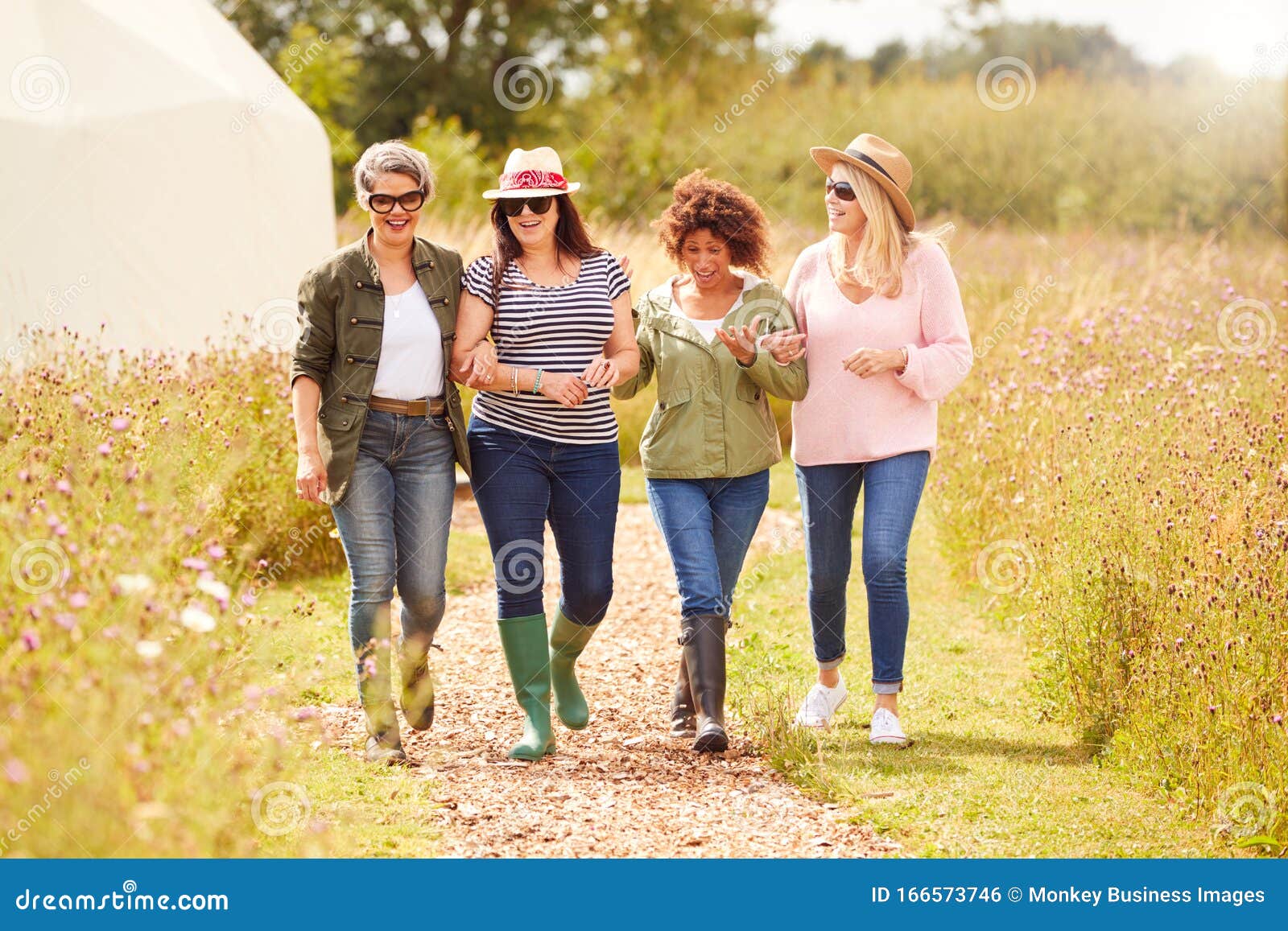 group of mature female friends walking along path through yurt campsite