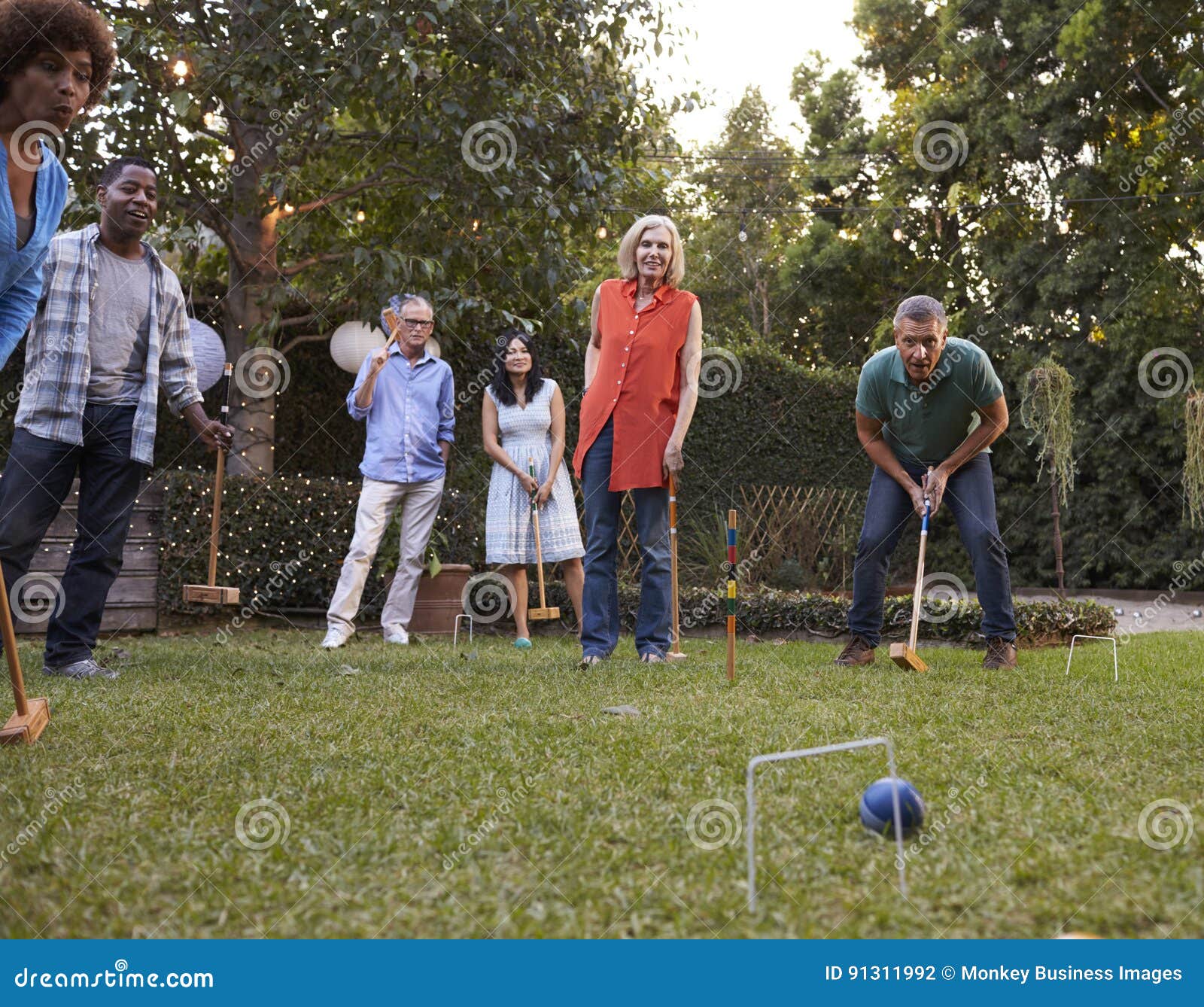 Group of Mature Friends Playing Croquet in Backyard Together Stock