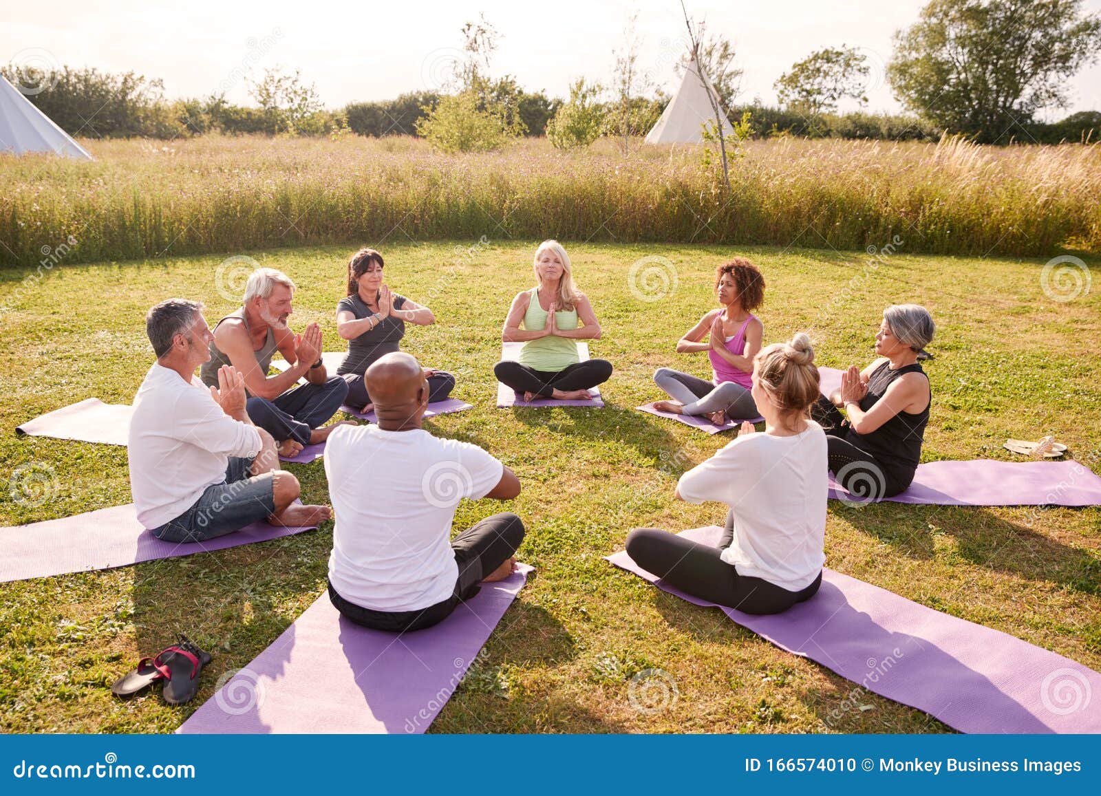 group of mature men and women in class at outdoor yoga retreat sitting circle meditating