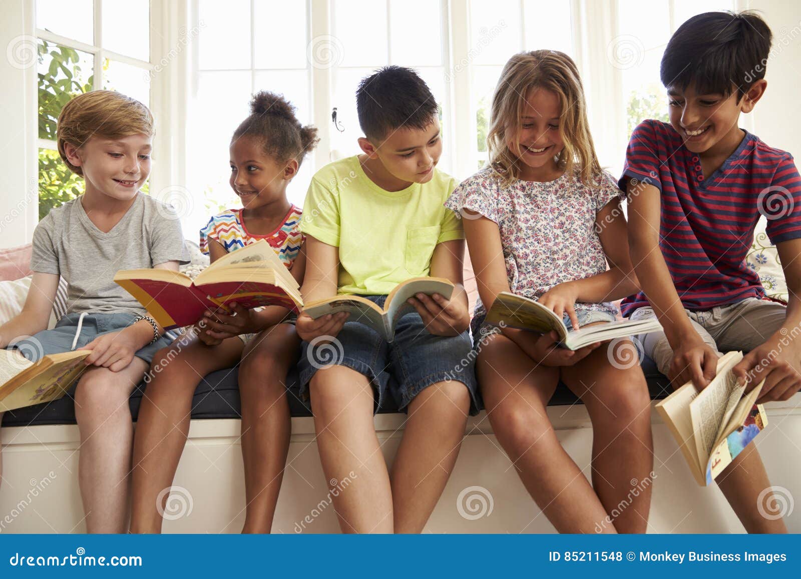 group of multi-cultural children reading on window seat