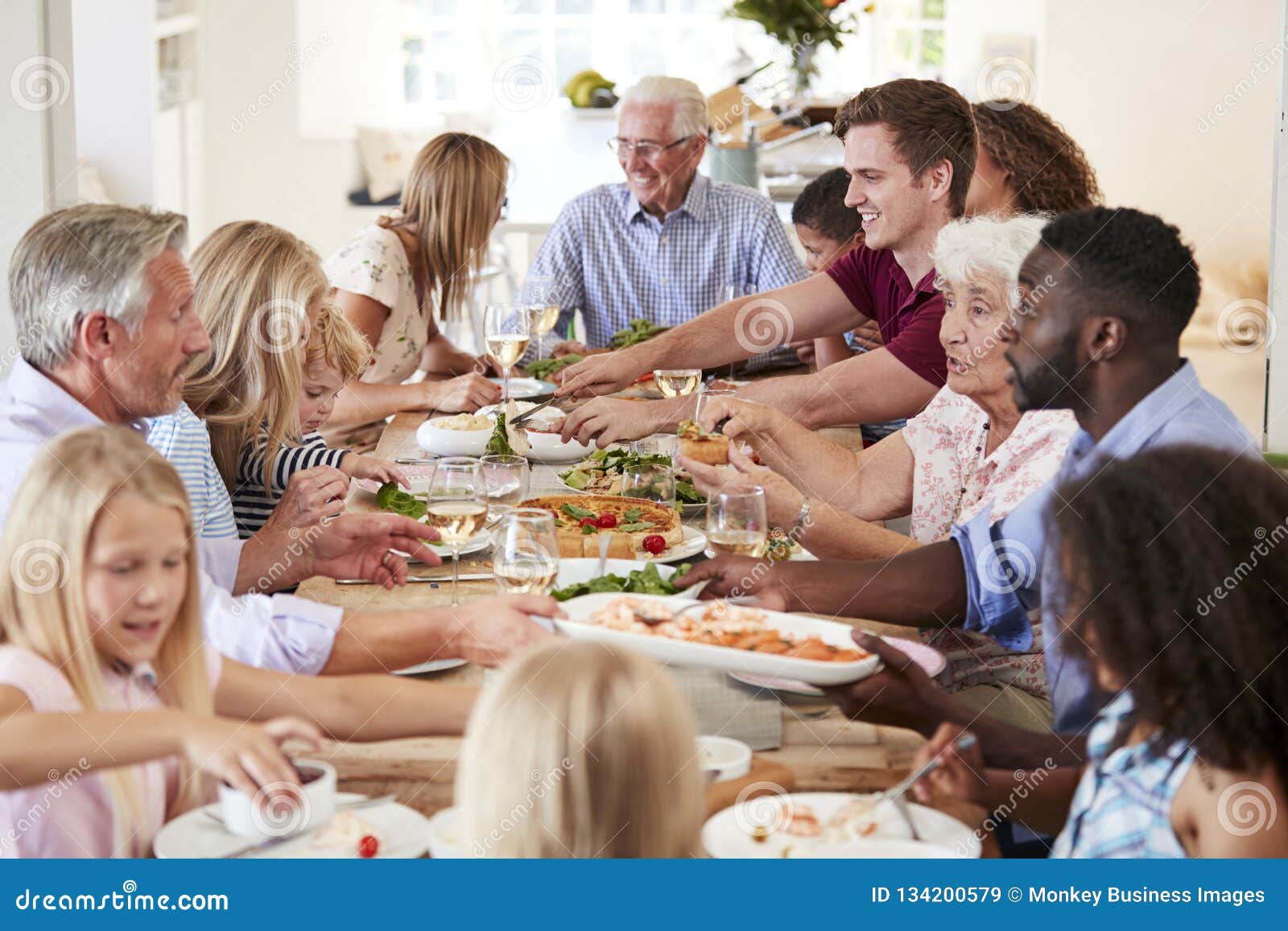group of multi-generation family and friends sitting around table and enjoying meal