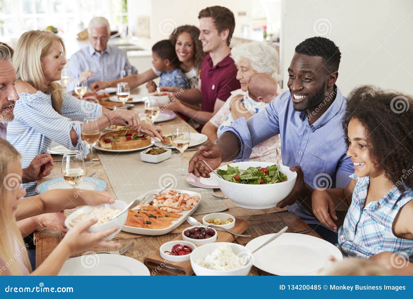 group of multi-generation family and friends sitting around table and enjoying meal