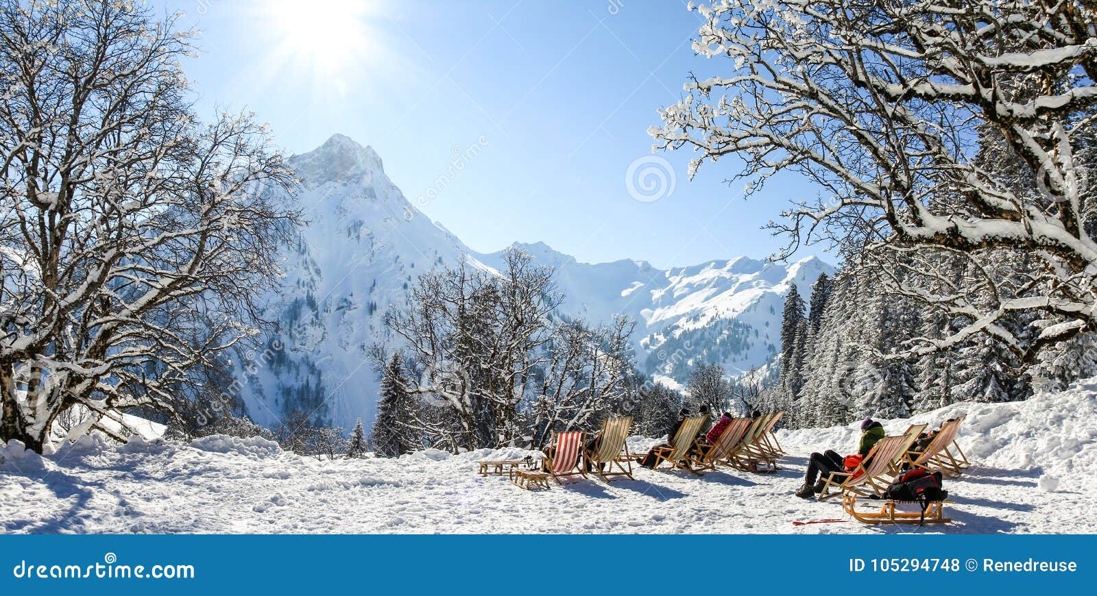 group of people sitting with deck chairs in winter mountains. sunbathing in snow. germany, bavaria, allgau