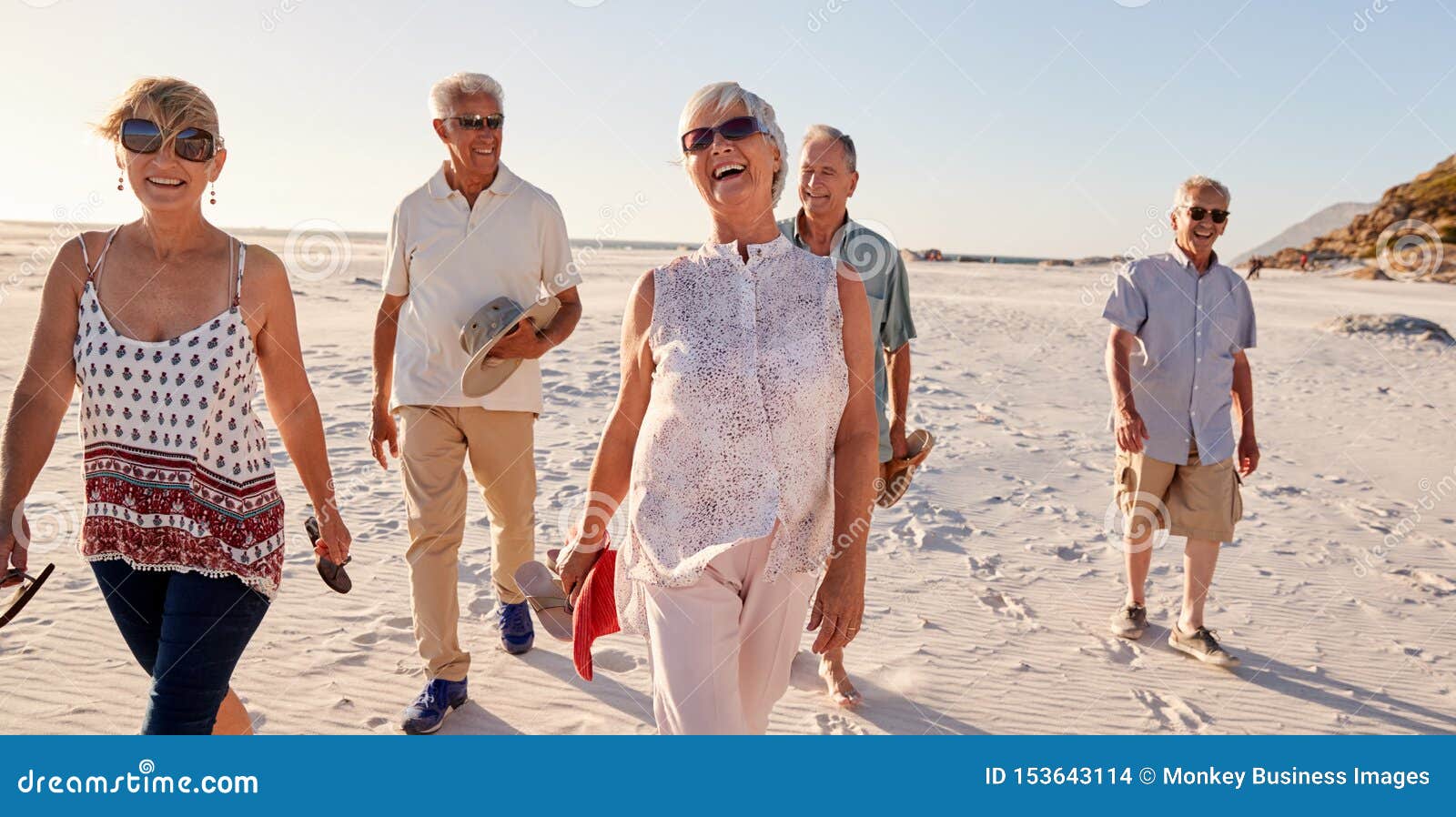 group of senior friends walking along sandy beach on summer group vacation