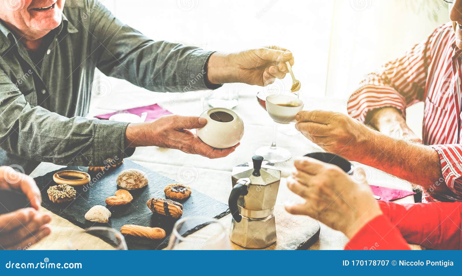 group of senior people toasting italian style moka coffee after lunch - mature happy friends eating biscuits and laughing together