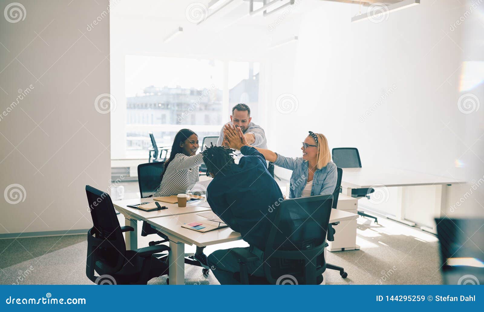 group of smiling colleagues high fiving during an office meeting