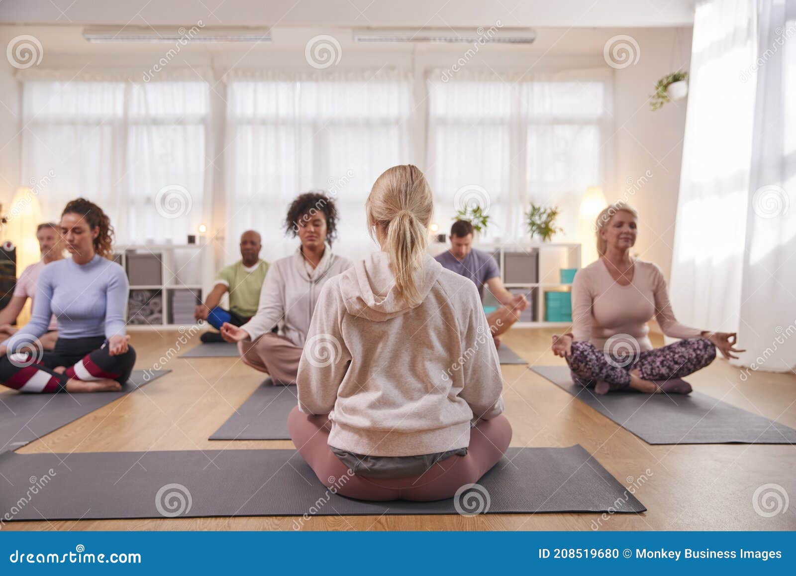 Group with Teacher Sitting on Exercise Mats Stretching in Yoga Class