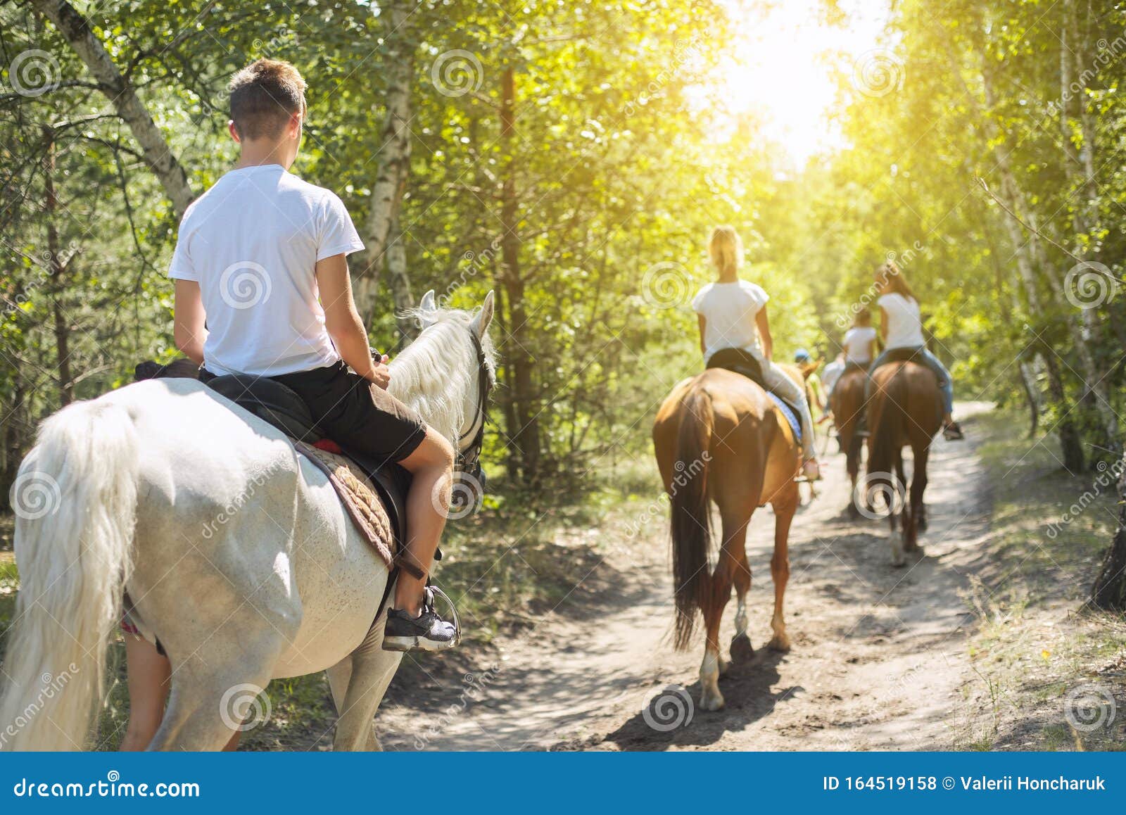 group of teenagers on horseback riding in summer park