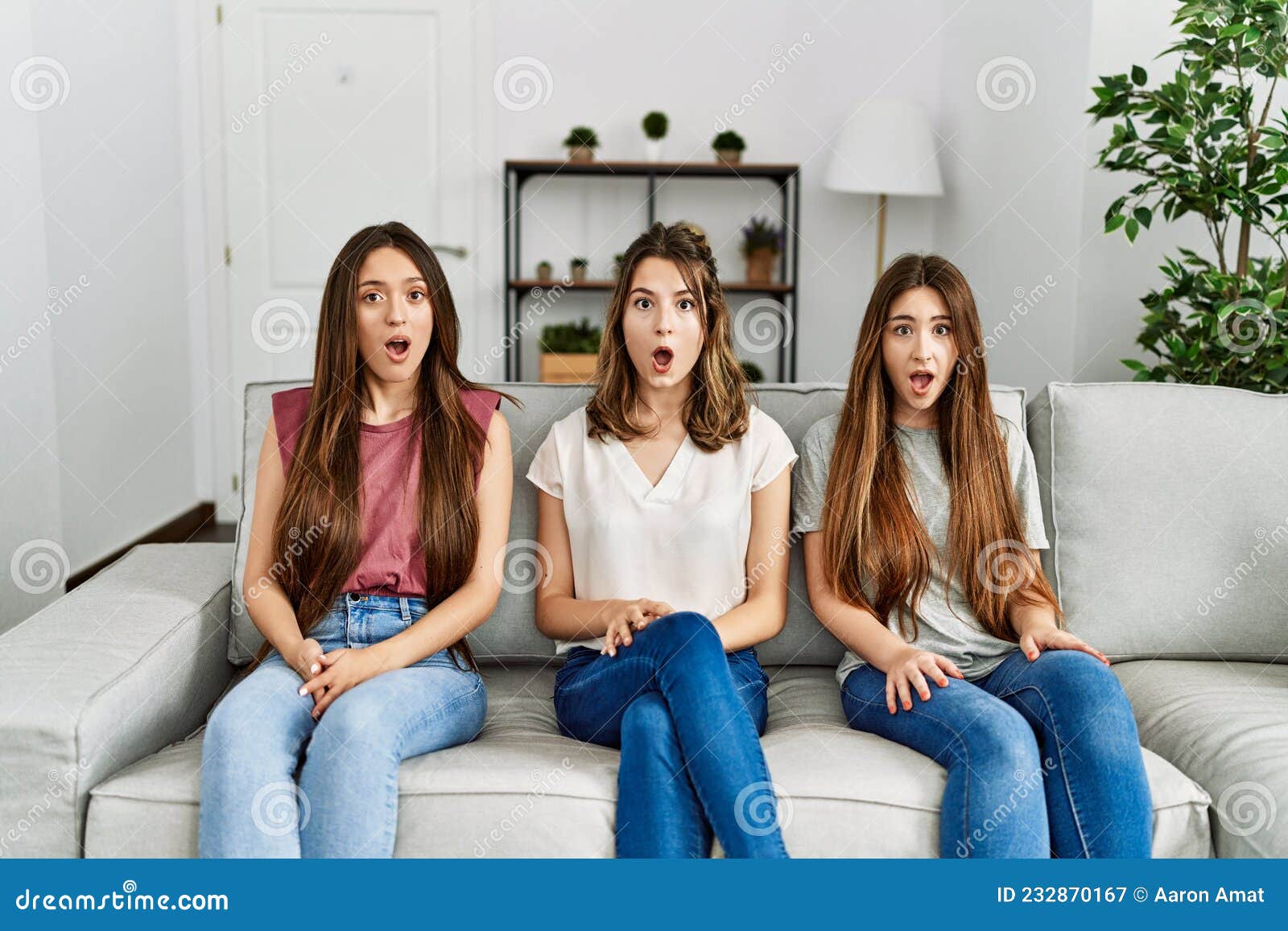Group Of Three Hispanic Girls Sitting On The Sofa At Home Afraid And Shocked With Surprise
