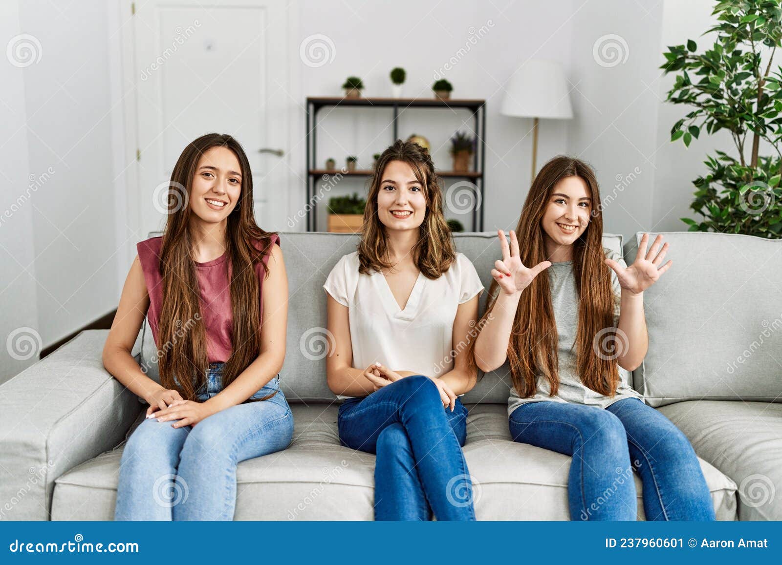 Group Of Three Hispanic Girls Sitting On The Sofa At Home Showing And