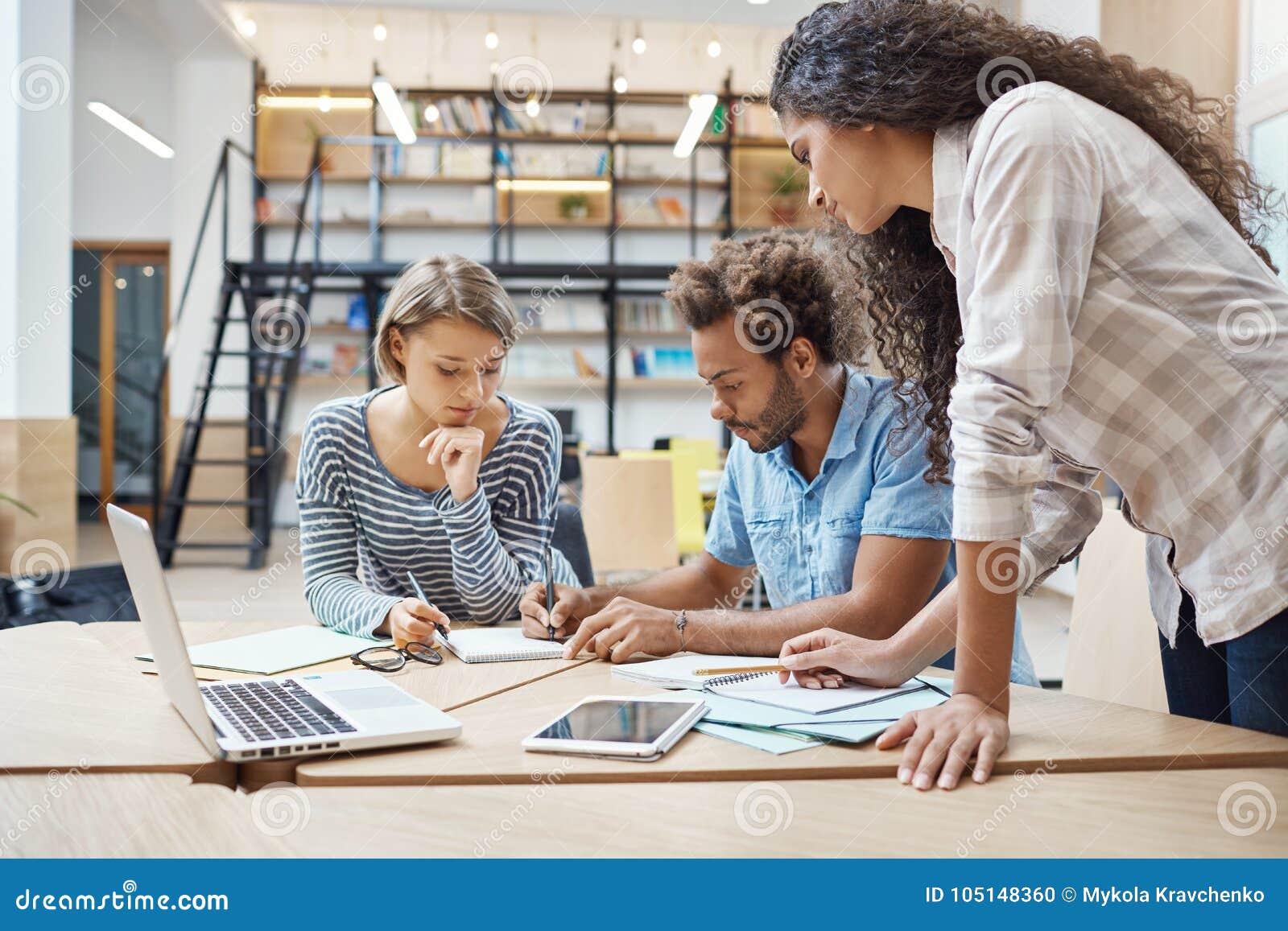 group of three young multi-ethnic successful business people sitting in coworking space, talking about new project of