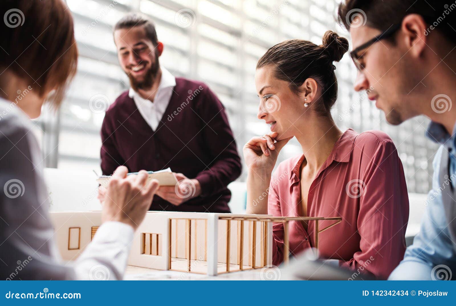 Group of Young Architects with Model of a House Standing in Office