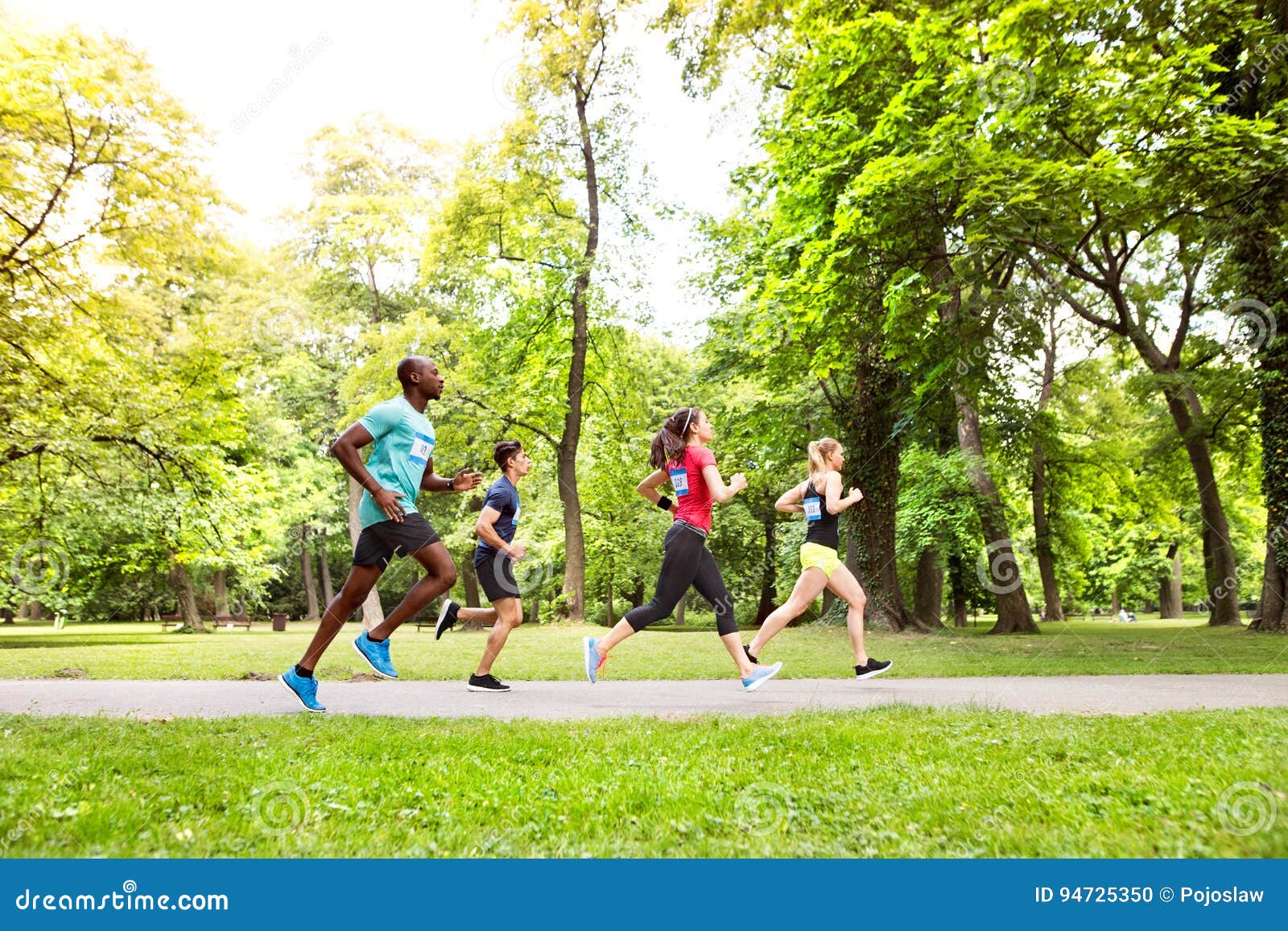 Group of Young Athletes Running in Green Sunny Park. Stock Photo