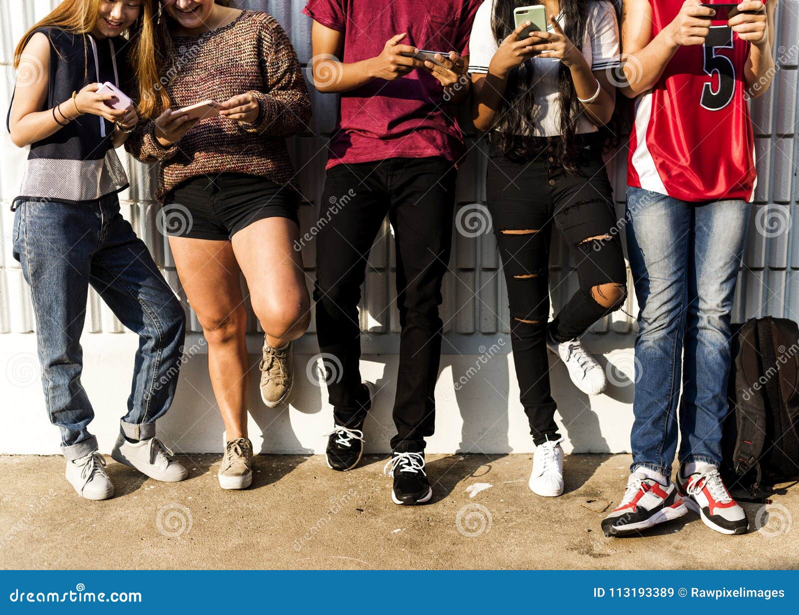 group of young teenager friends chilling out together using smartphone social media concept