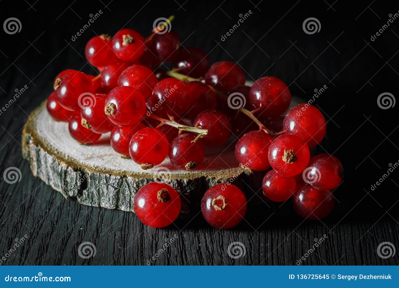 Groupe mûr de groseilles rouges sur une coupe d'un arbre, fond foncé. Groupe mûr de groseilles fraîches sur une coupe d'un arbre, fond en bois foncé