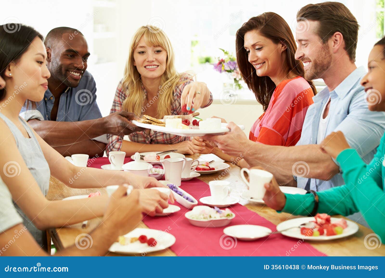 Grupo de amigos que comem o queijo e o café no partido de jantar que senta-se em torno da tabela que ajuda-se ao alimento