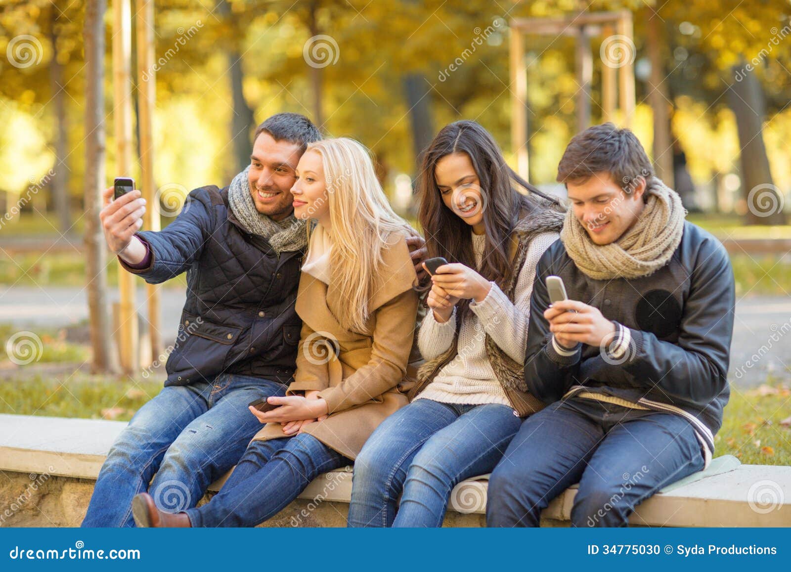 Grupo de amigos que se divierten en parque del otoño. Verano, días de fiesta, vacaciones, concepto feliz de la gente - grupo de amigos o pares con el smartphone que se divierte en parque del otoño