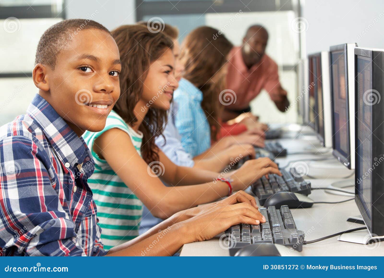 Grupo de estudantes que trabalham em computadores na sala de aula que olha o sorriso da câmera