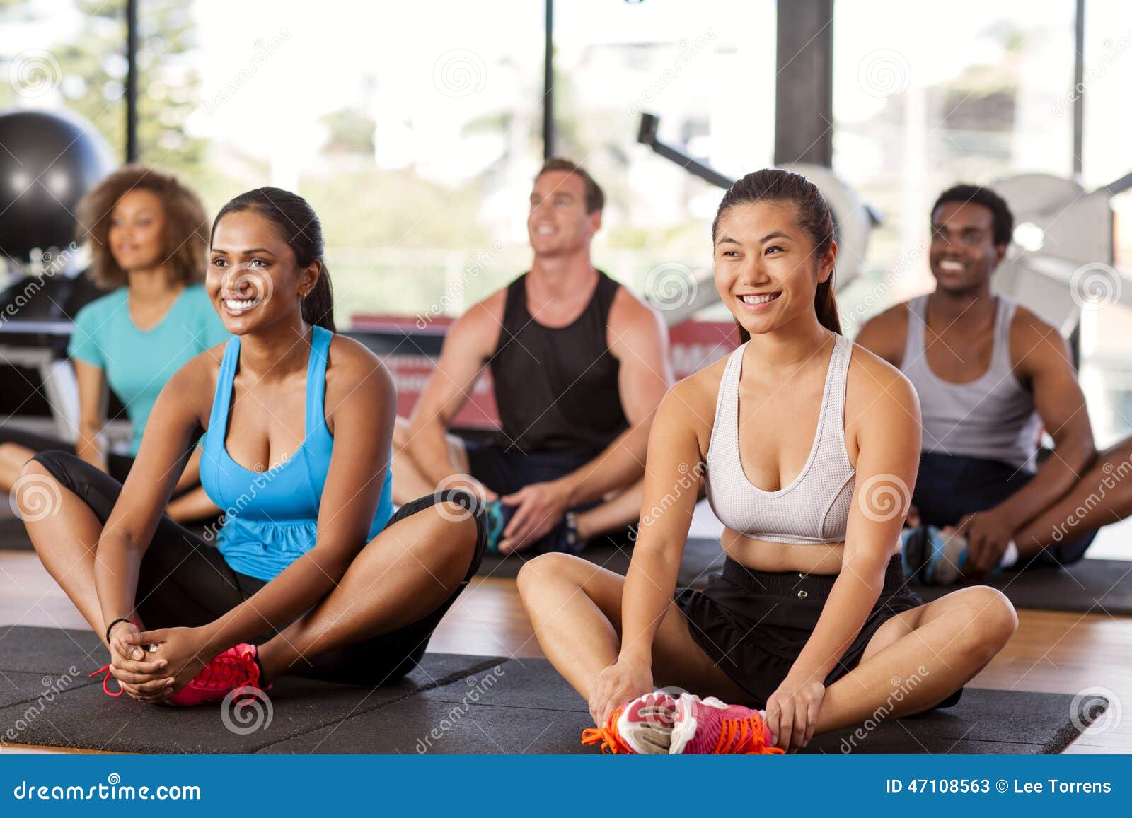 Grupo Multi-étnico que estica em um gym antes de sua classe do exercício