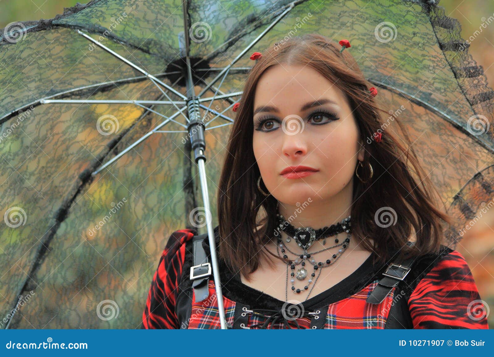 Guarda-chuva gótico II. Modelo gótico com as rosas marrons do olho e do vermelho em seu cabelo sob um guarda-chuva.