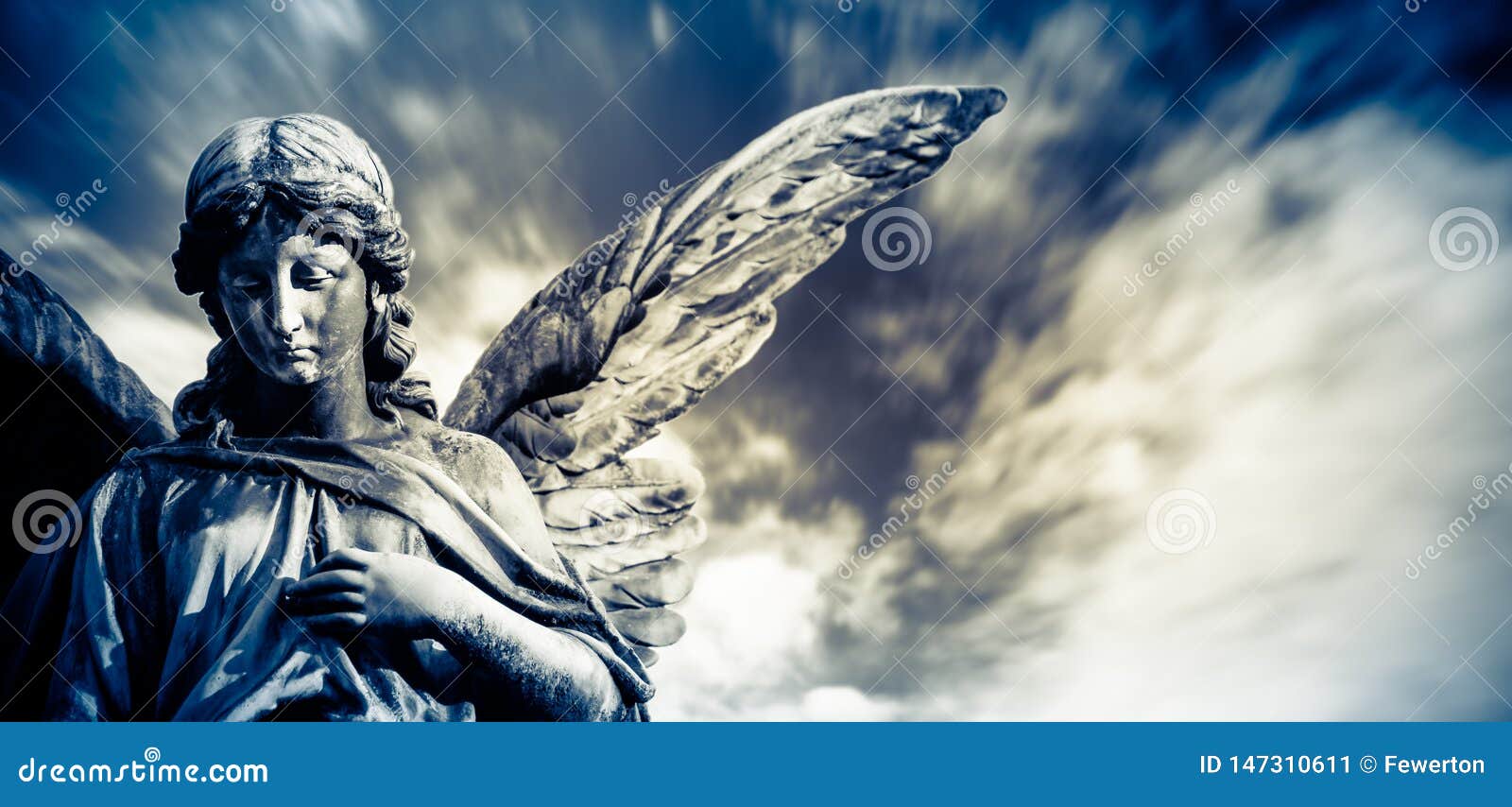 guardian angel sculpture with open long wings  with blurred white clouds dramatic light blue sky. angel sad expression