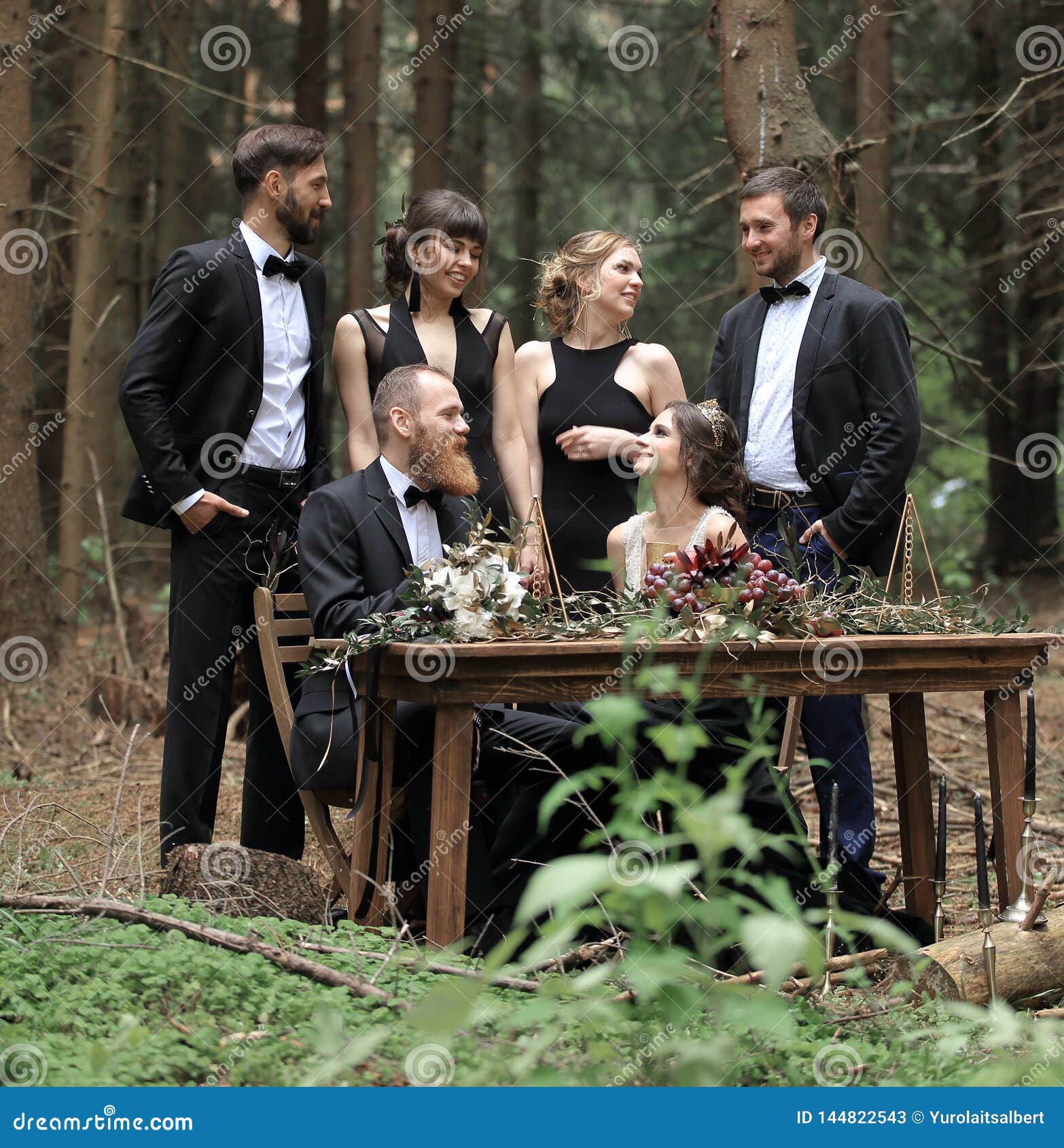 Guests And A Couple Of Newlyweds Near The Picnic Table In The Woods