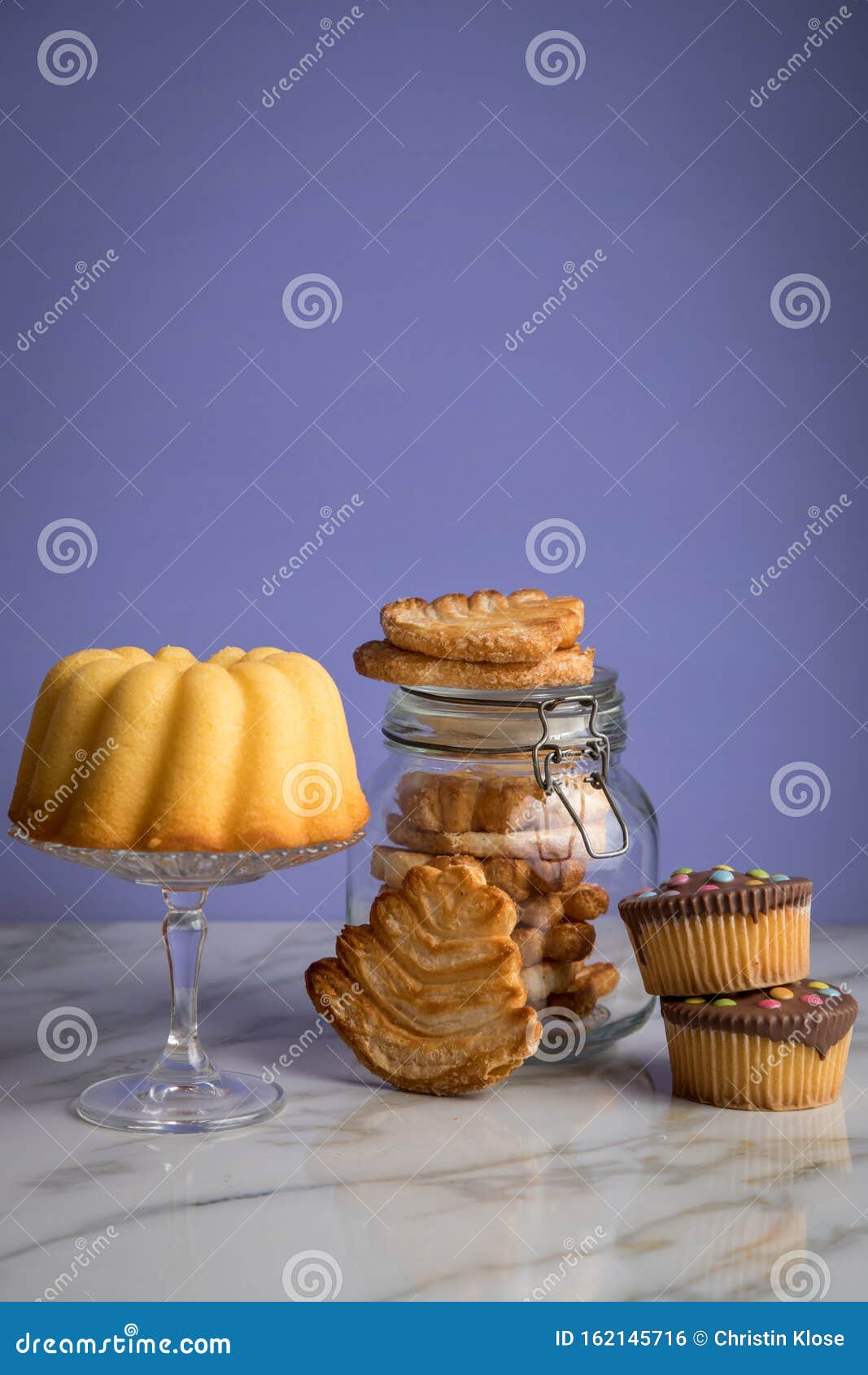 gugelhupf ring cake, muffins, italian puff pastry fan wavers cookies biscuits as selection buffet on marble table and lilac