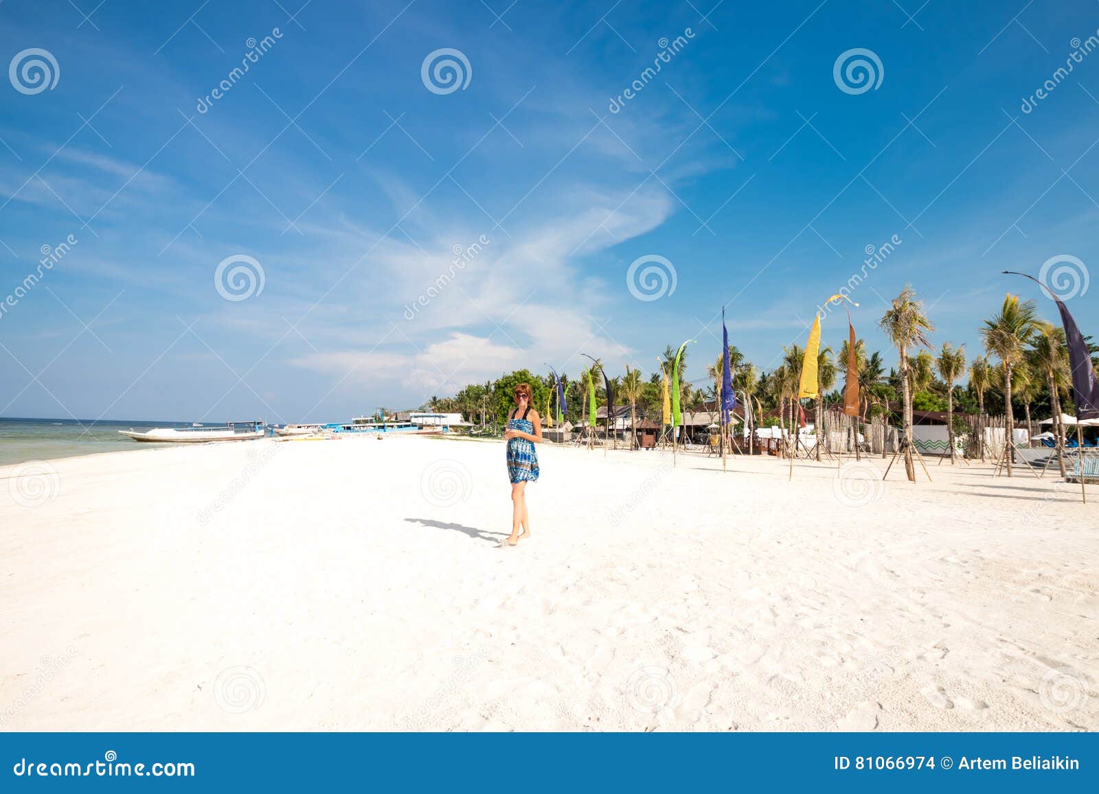 Gullig stilfull flicka i blåttklänninganseende på den fantastiska stranden med witesand, hållande smartphone i henne händer Hon har på brun solglasögon Hav bak henne