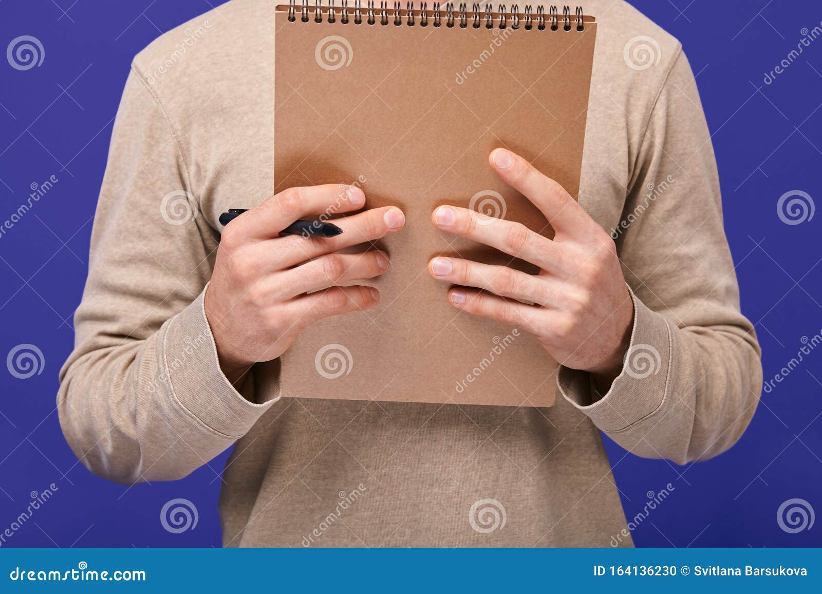 the guy`s hands holding ballpoint pen and brown draft notebook