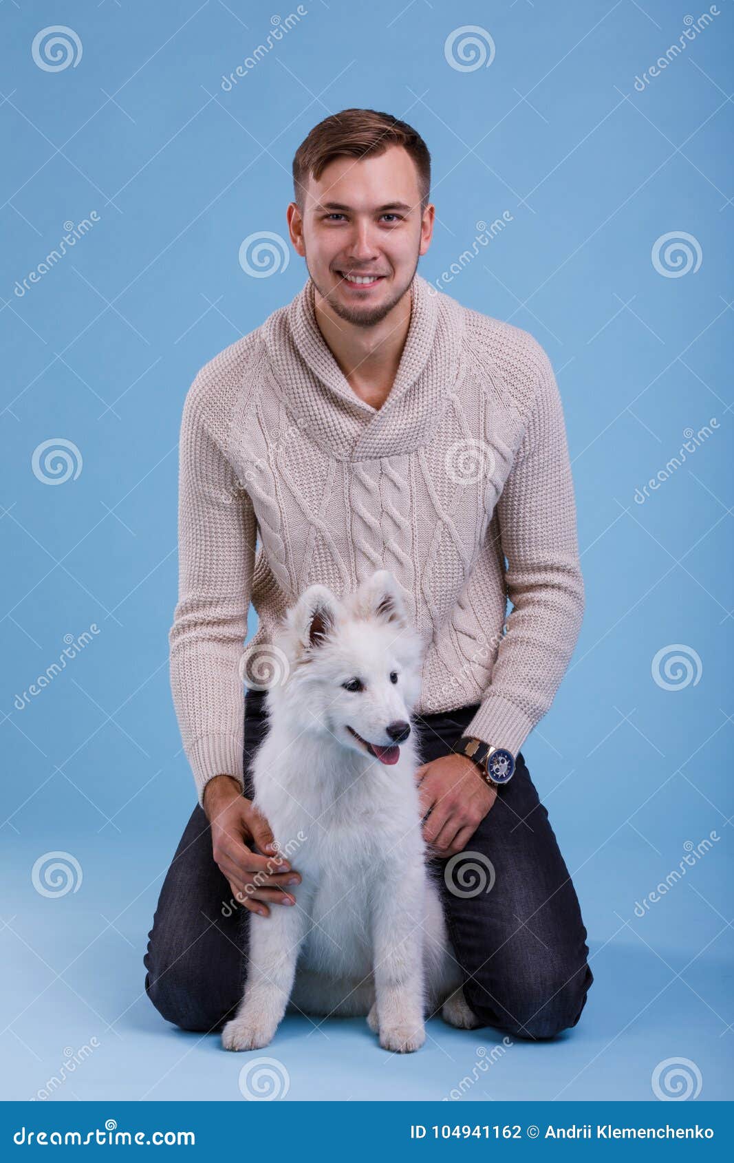 a guy sits next to a samoyed puppy. on a blue background.