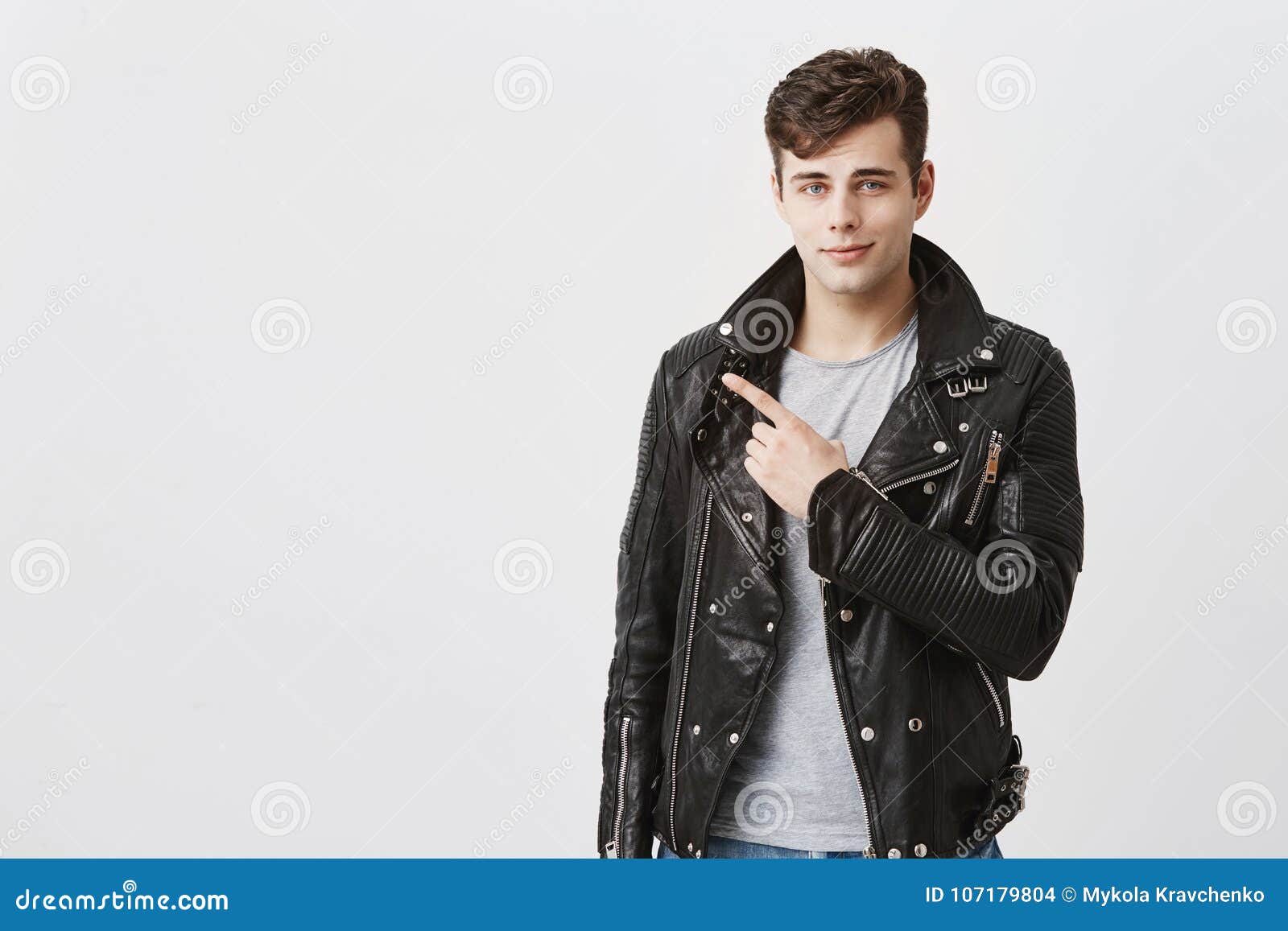 guy smiling gently in black leather jacket indicates with fore finger at copy space for advertisment or promotional text