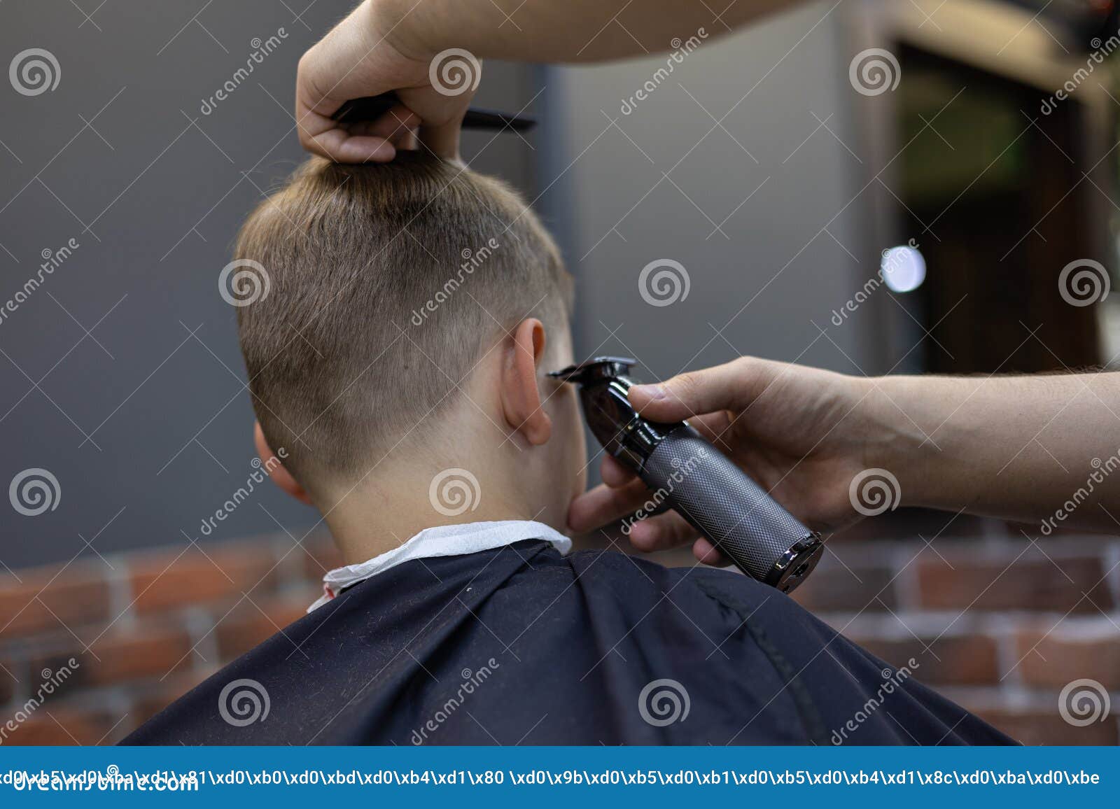 the hairdresser flattens the hair on the temples of a child boy. the boy trusts the hairdresser and sits calmly in the
