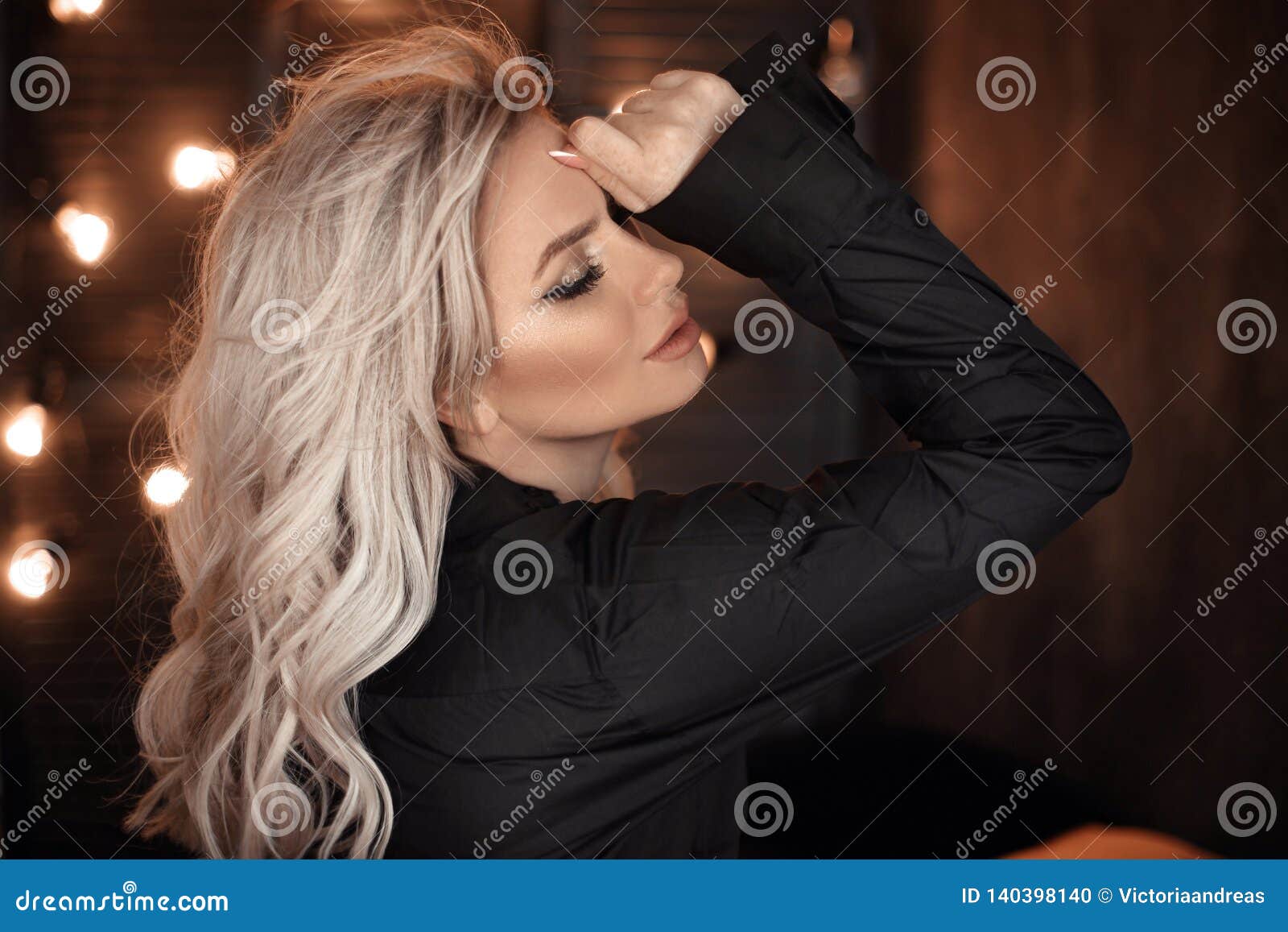 hairstyle. beautiful blonde woman portrait posing in black shirt. fashionable blond girl model over bokeh lights dark background