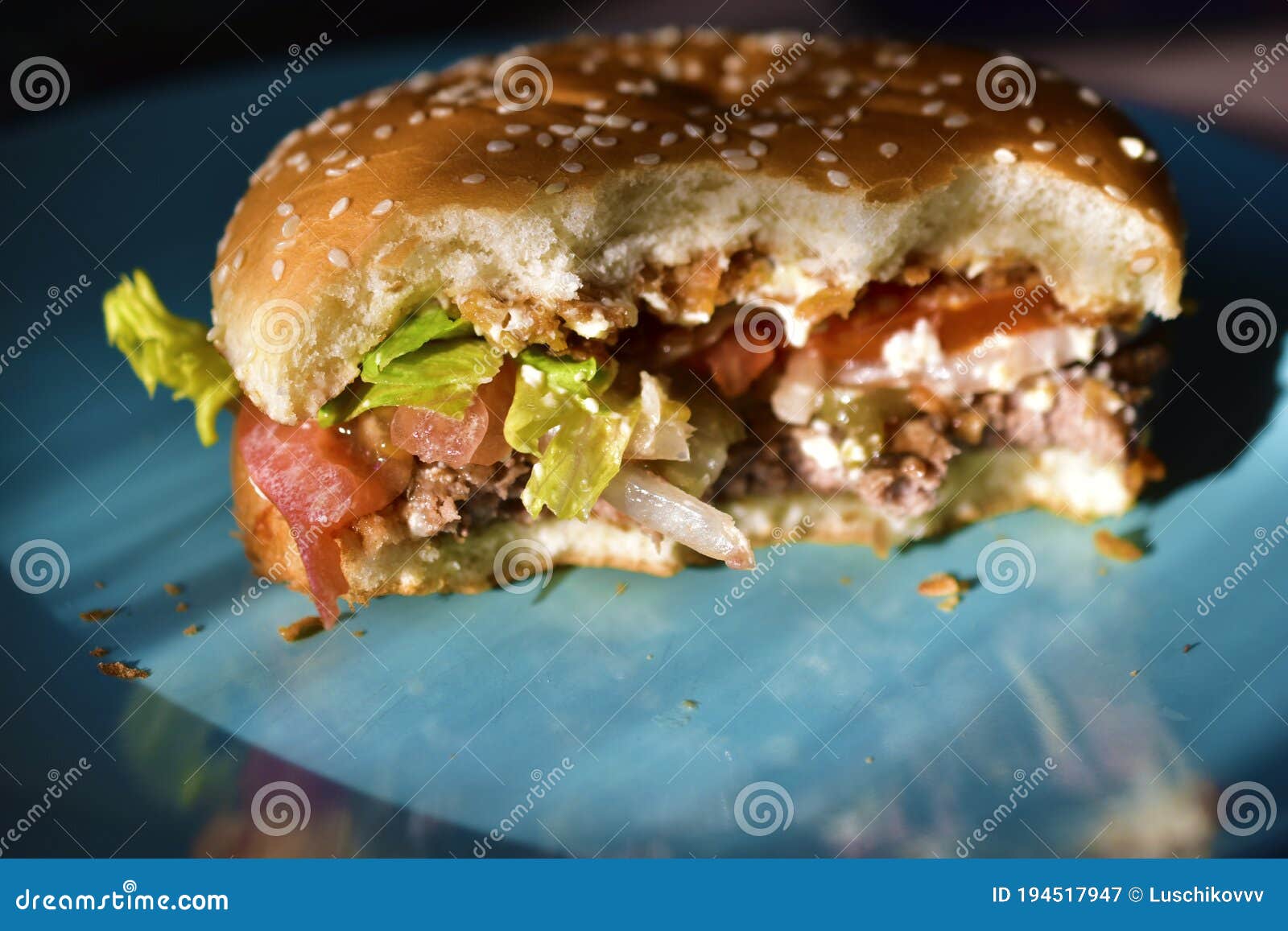 A Halfeaten Meat Burger with Vegetables on a Blue Plate Stock Image