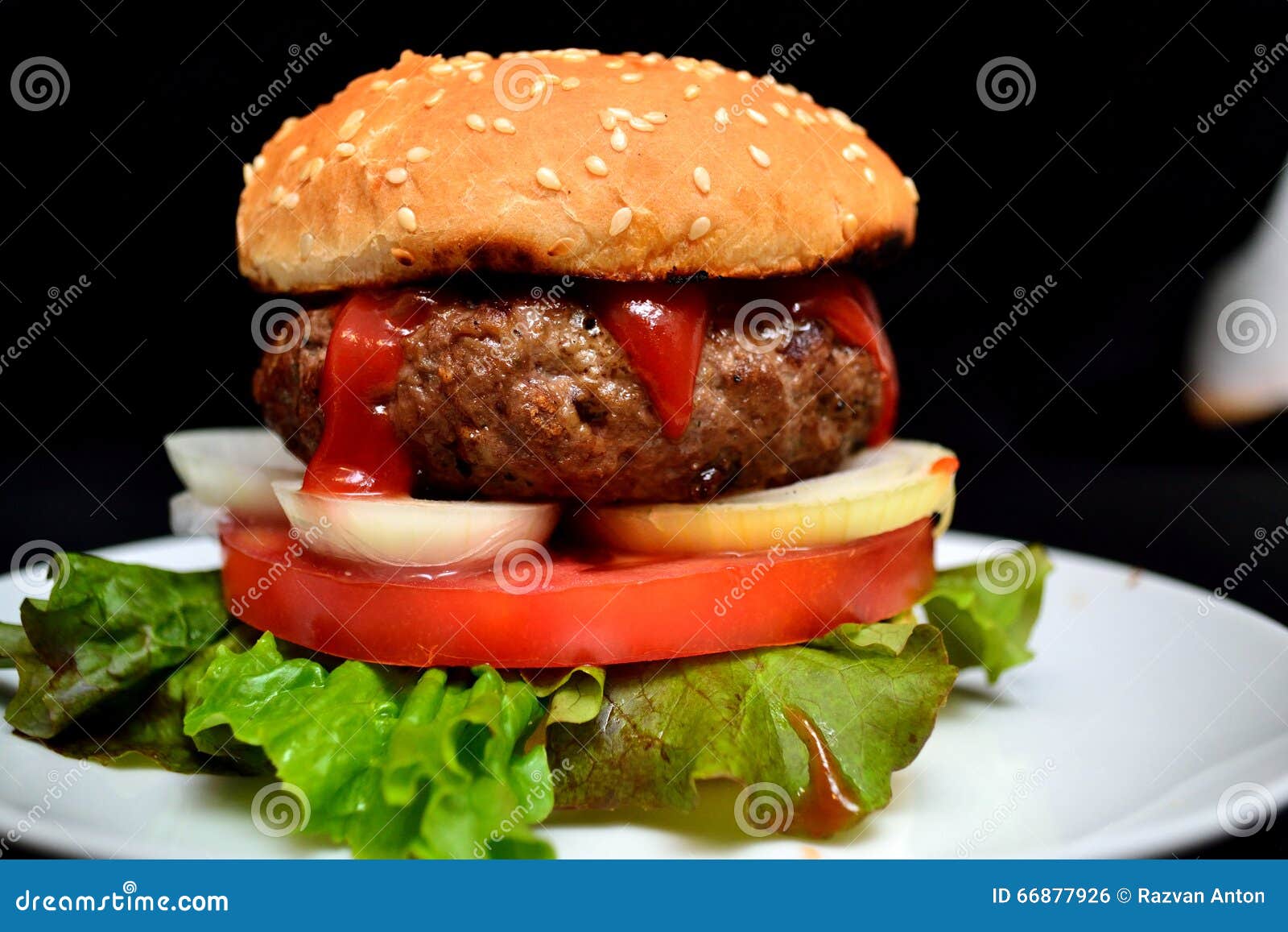 Hamburger de veau avec de la salade. Hamburger de veau et de boeuf avec de la salade, l'oignon et la tomate d'un plat blanc et d'un fond noir