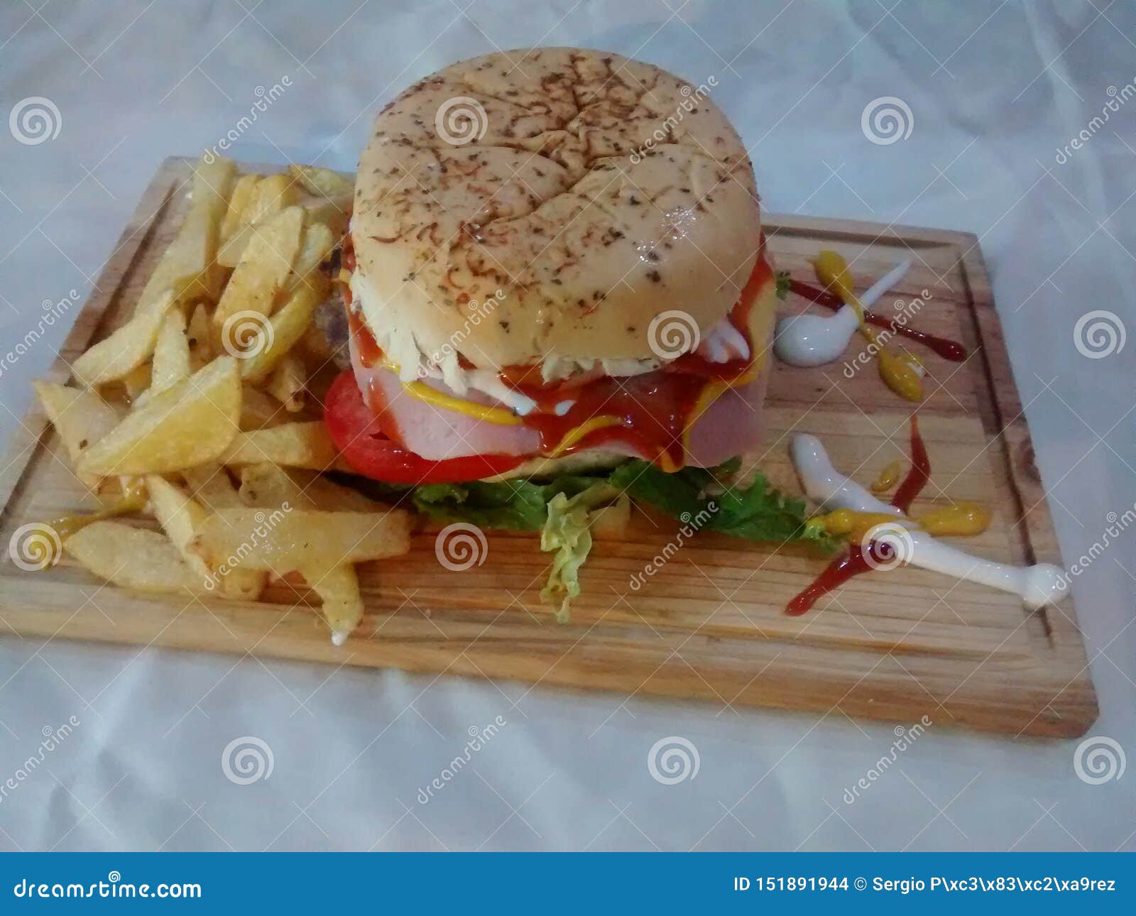 hamburger on wooden table with fried potatoes and sauces of various colors and flavors is a fast or chatarra food