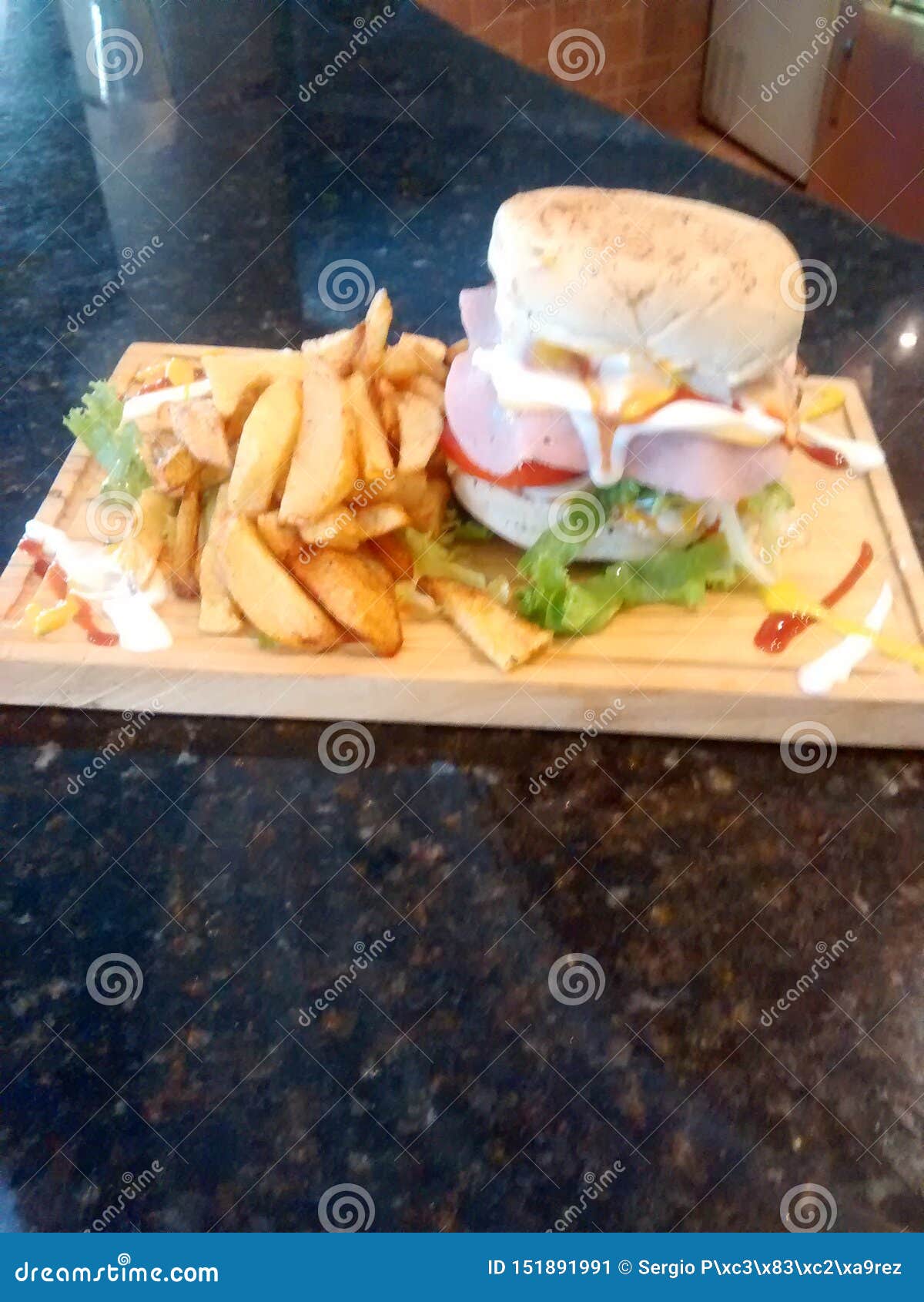 hamburger on wooden table with fried potatoes and sauces of various colors and flavors is a fast or chatarra food