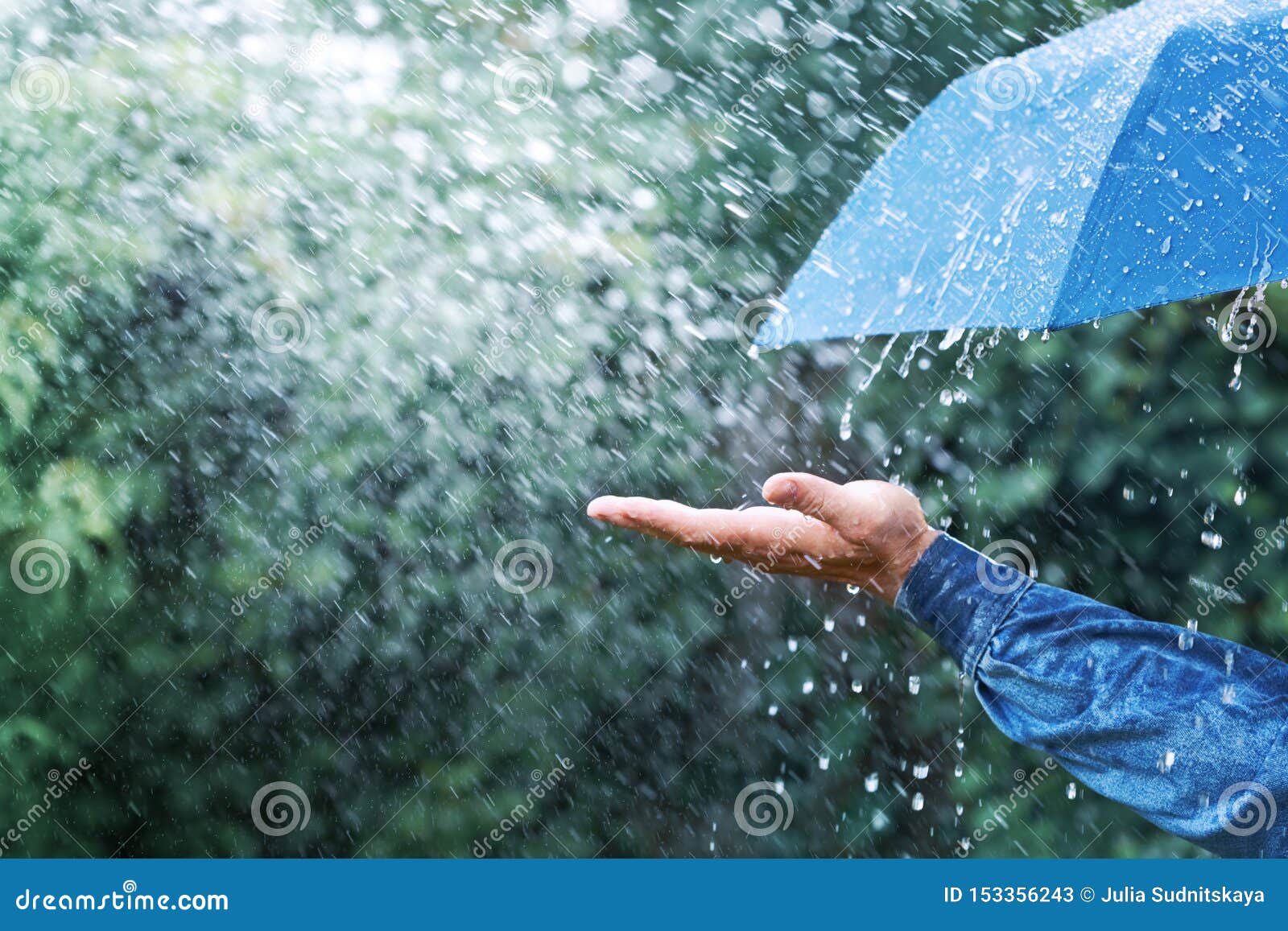 hand and blue umbrella under heavy rain against nature background. rainy weather concept